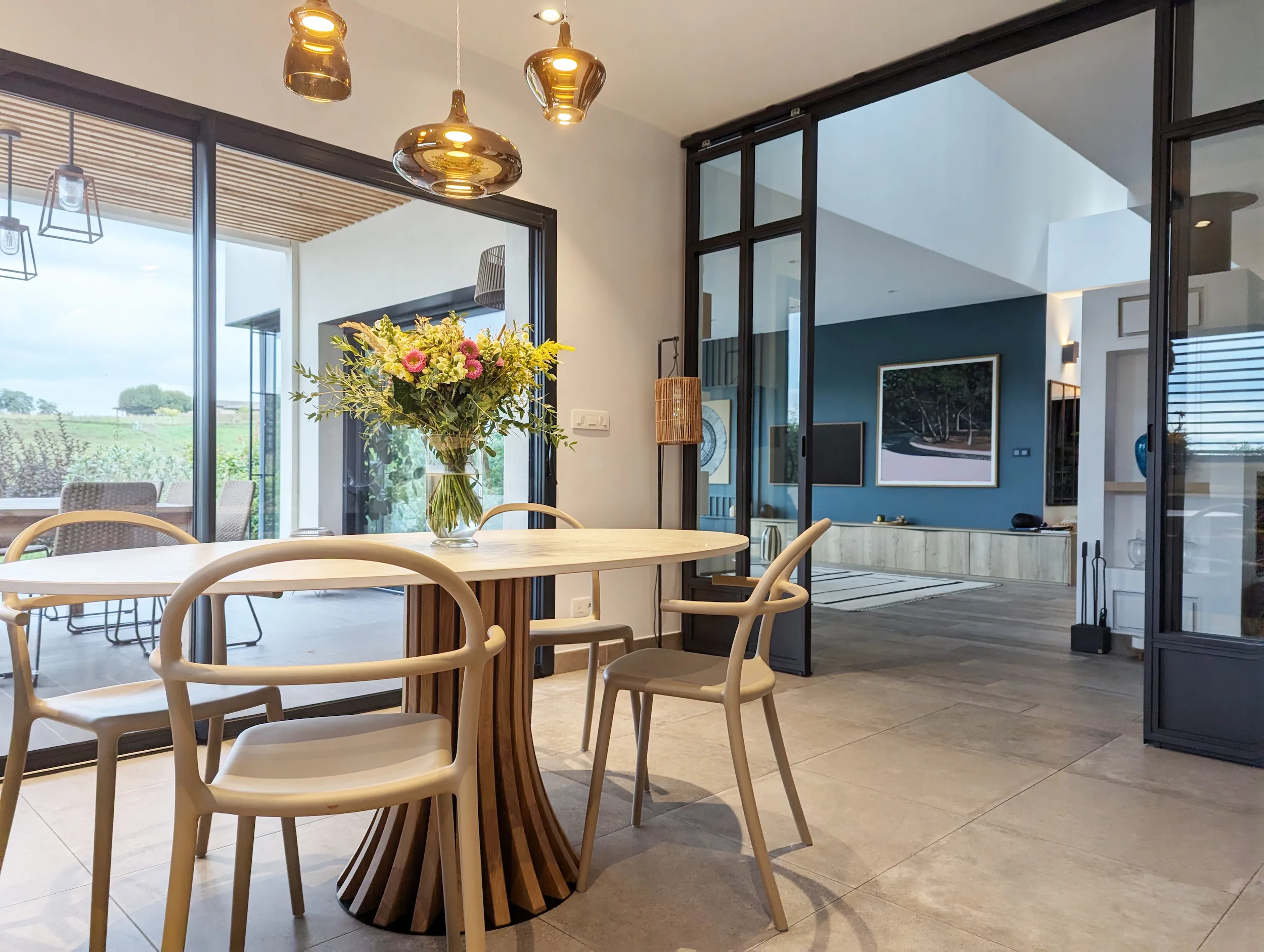 Salle à manger contemporaine mêlant bois clair, suspensions dorées et vue traversante jusqu’au salon imaginé par Valentine Bourdier.