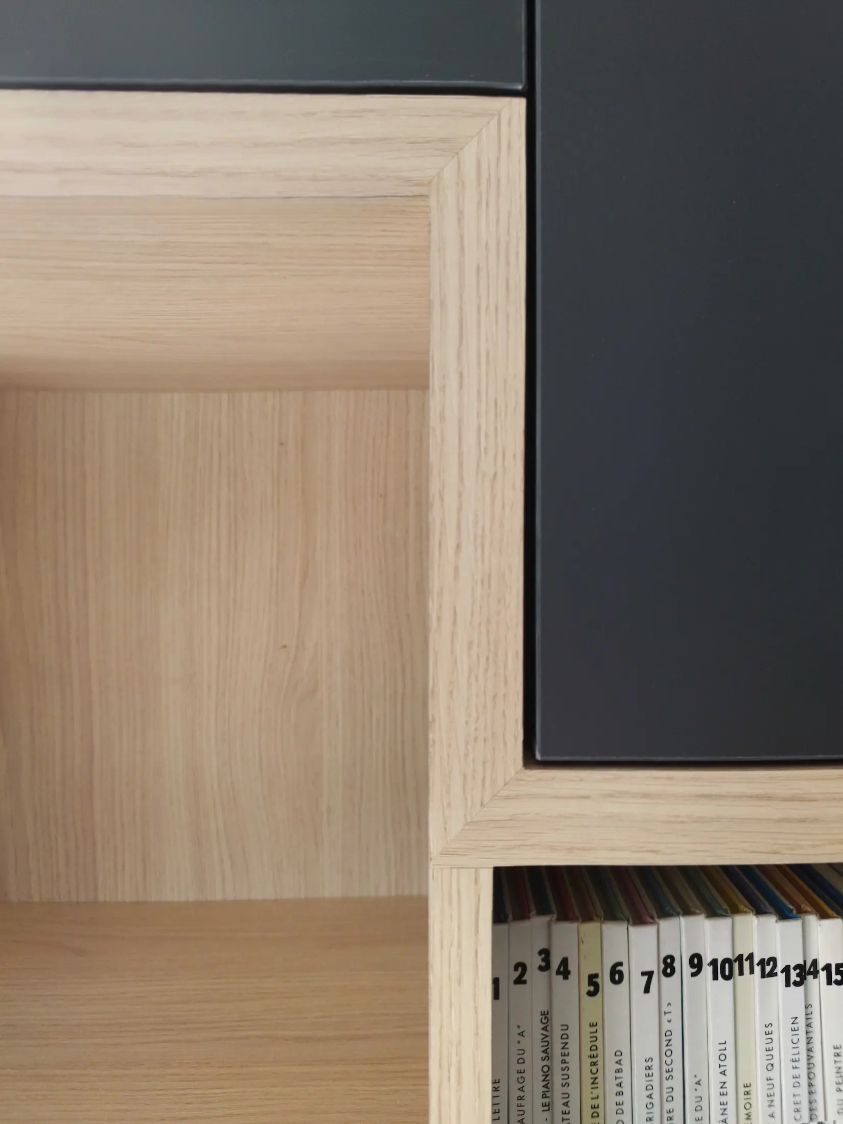 Détail d’une bibliothèque sur mesure en bois clair avec niches ouvertes et rangements intégrés.
