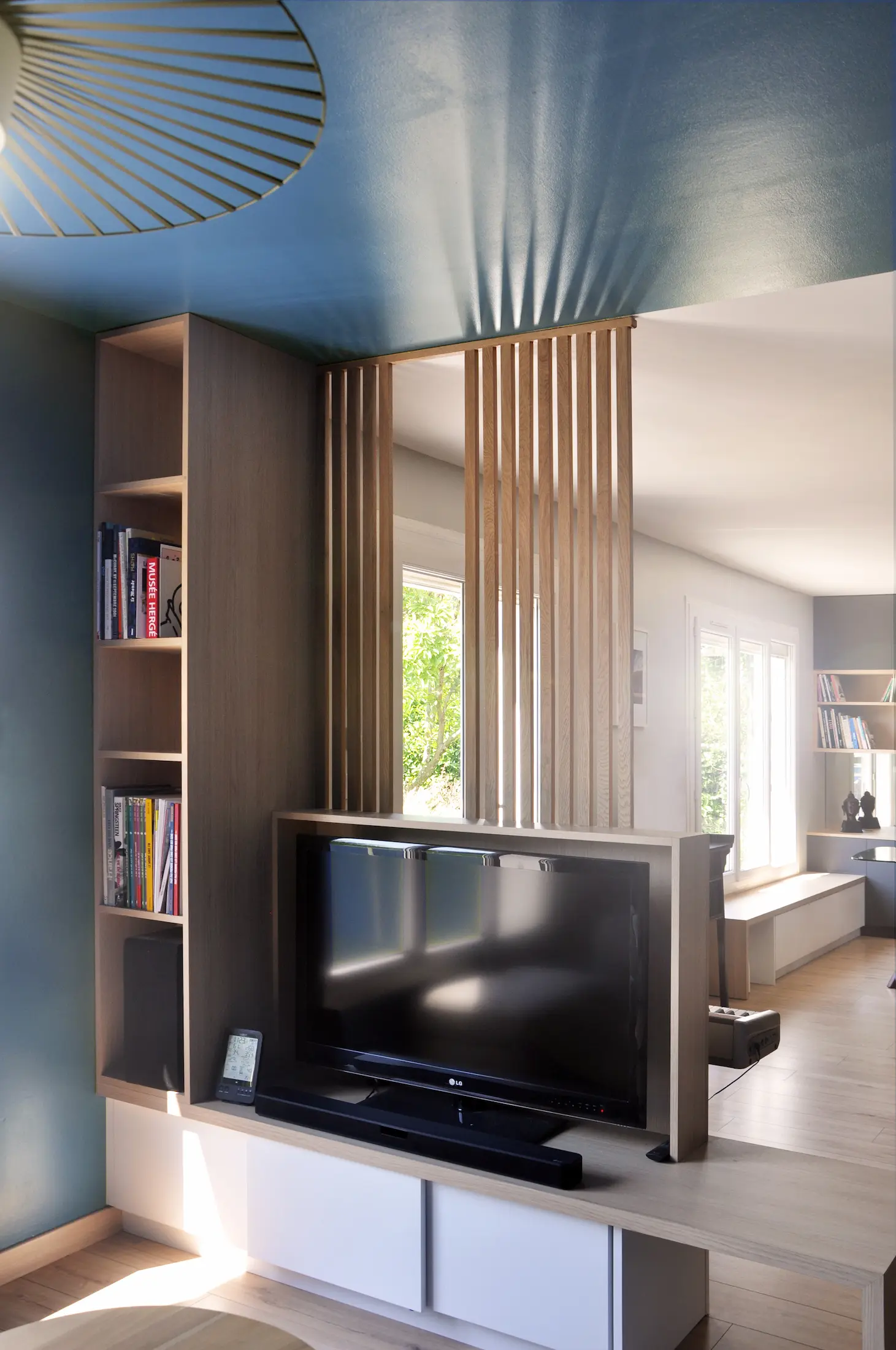 Claustra en bois intégrant un meuble TV et des rangements, séparation légère entre les espaces.