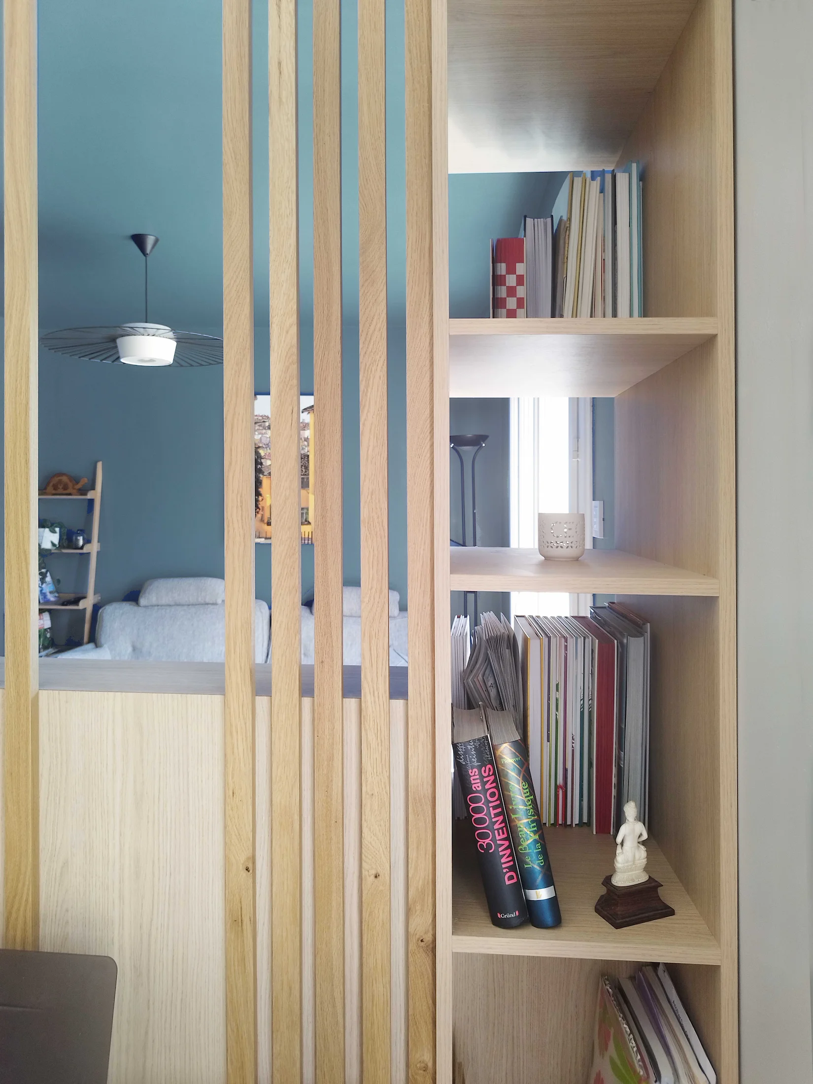 Claustra en bois avec étagères intégrées et livres, séparant les espaces d’une pièce de vie réaménagée.