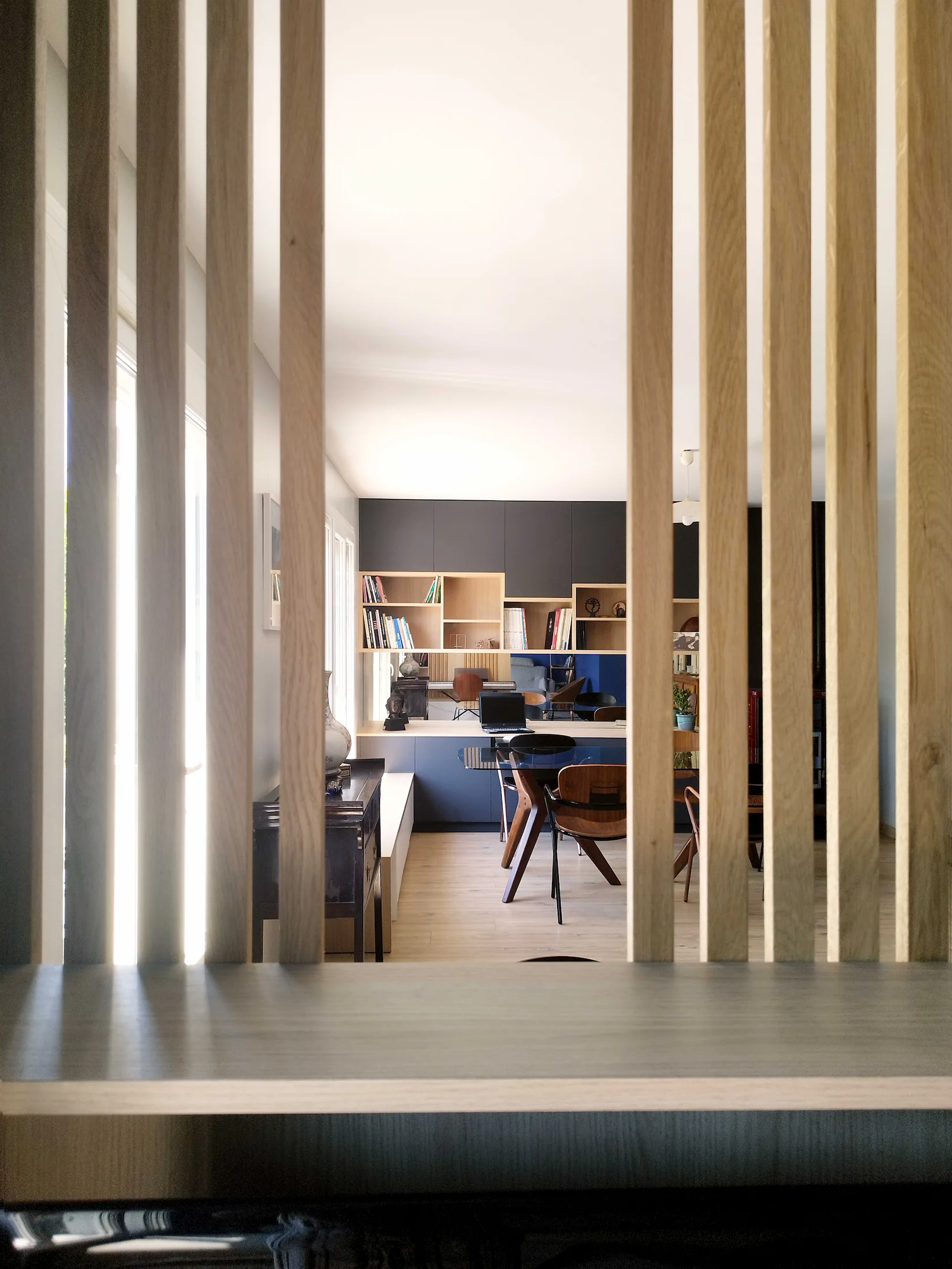 Vue à travers un claustra en bois ouvrant sur une pièce de vie avec mobilier et rangements sur mesure.