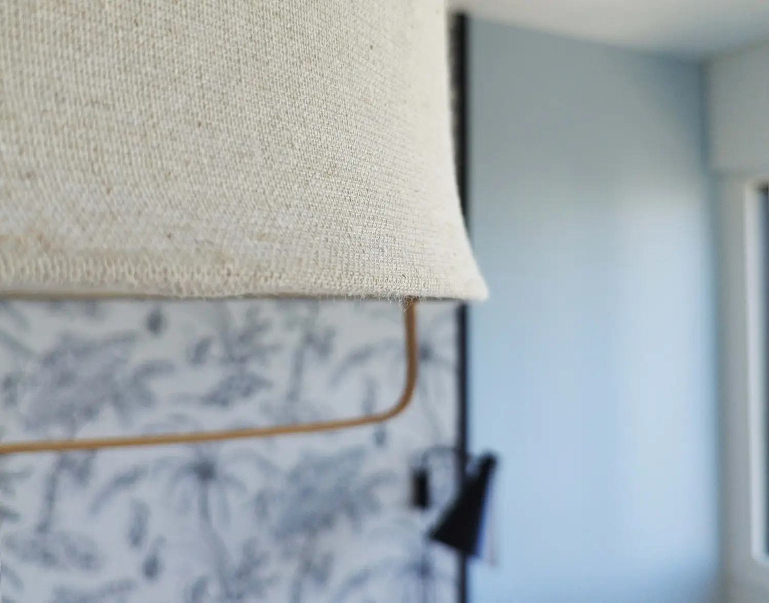 Gros plan sur une suspension textile au-dessus de la tête de lit, dans une chambre rénovée au style épuré avec papier peint botanique.
