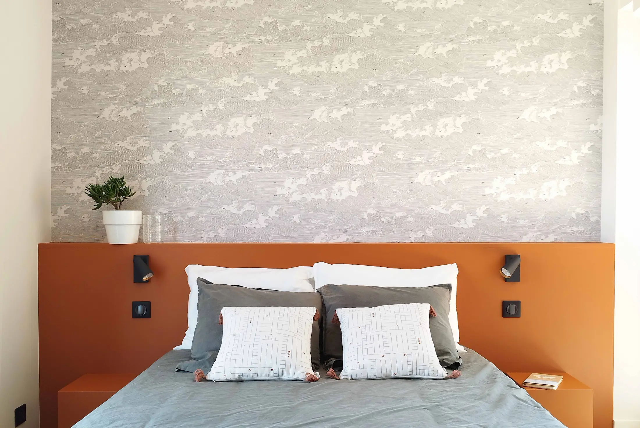 Tête de lit terracotta et jeu de coussins graphiques dans une chambre modernisée au style chaleureux.