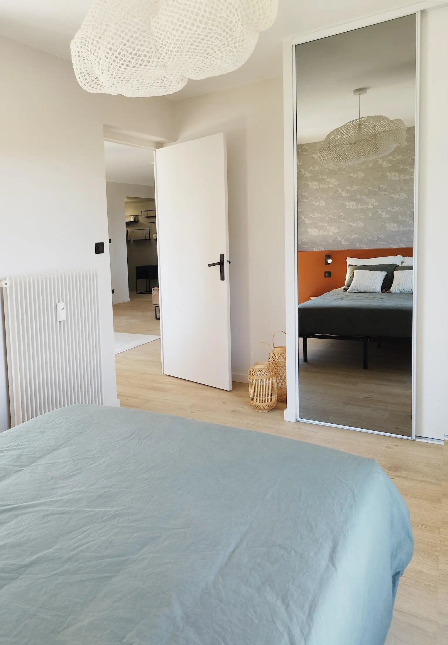 Chambre rénovée avec tête de lit colorée et vue sur l’espace nuit reflété dans le miroir du dressing.