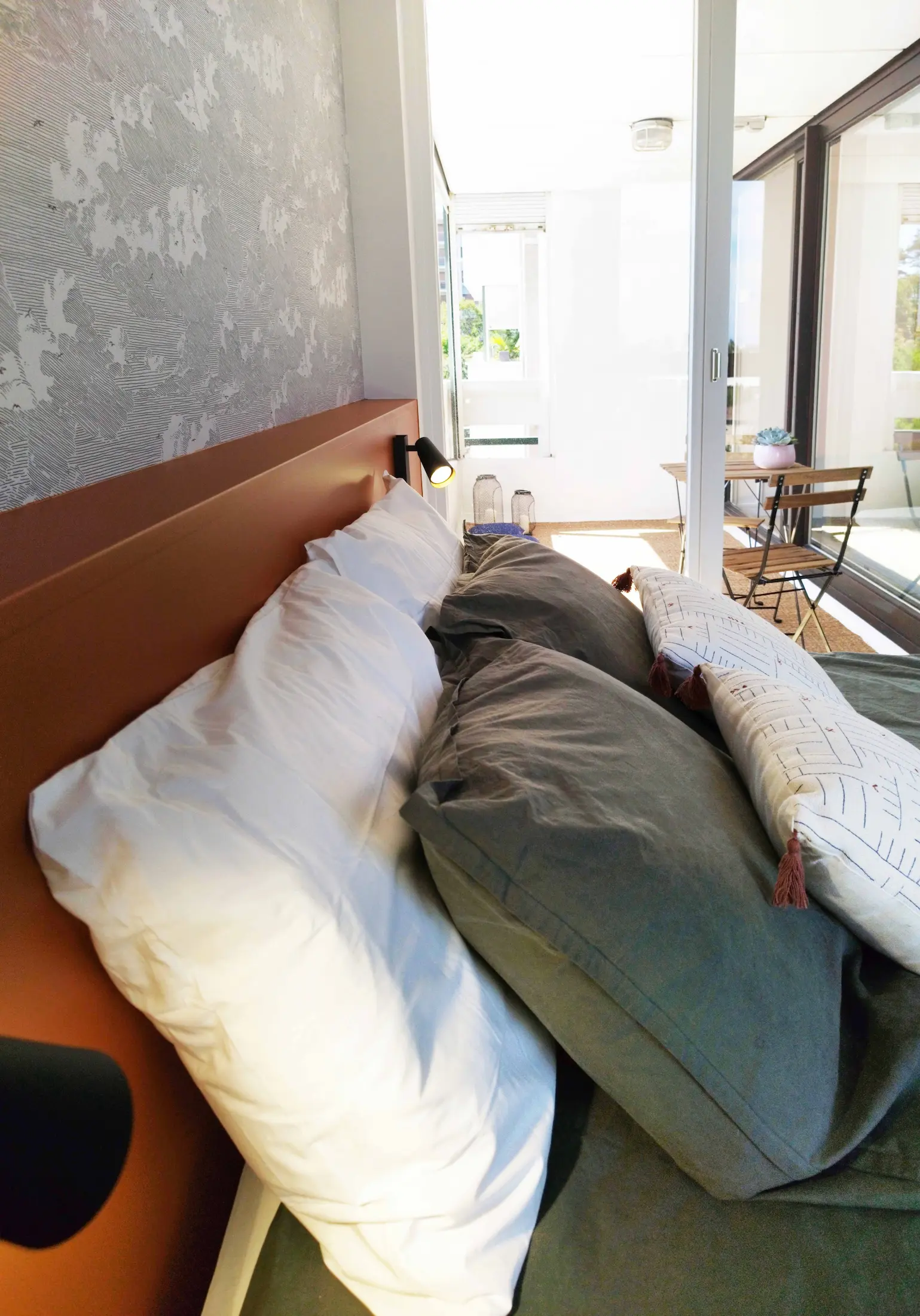 Jeu de coussins dans une chambre lumineuse donnant sur une loggia réaménagée, ambiance douce et contemporaine.