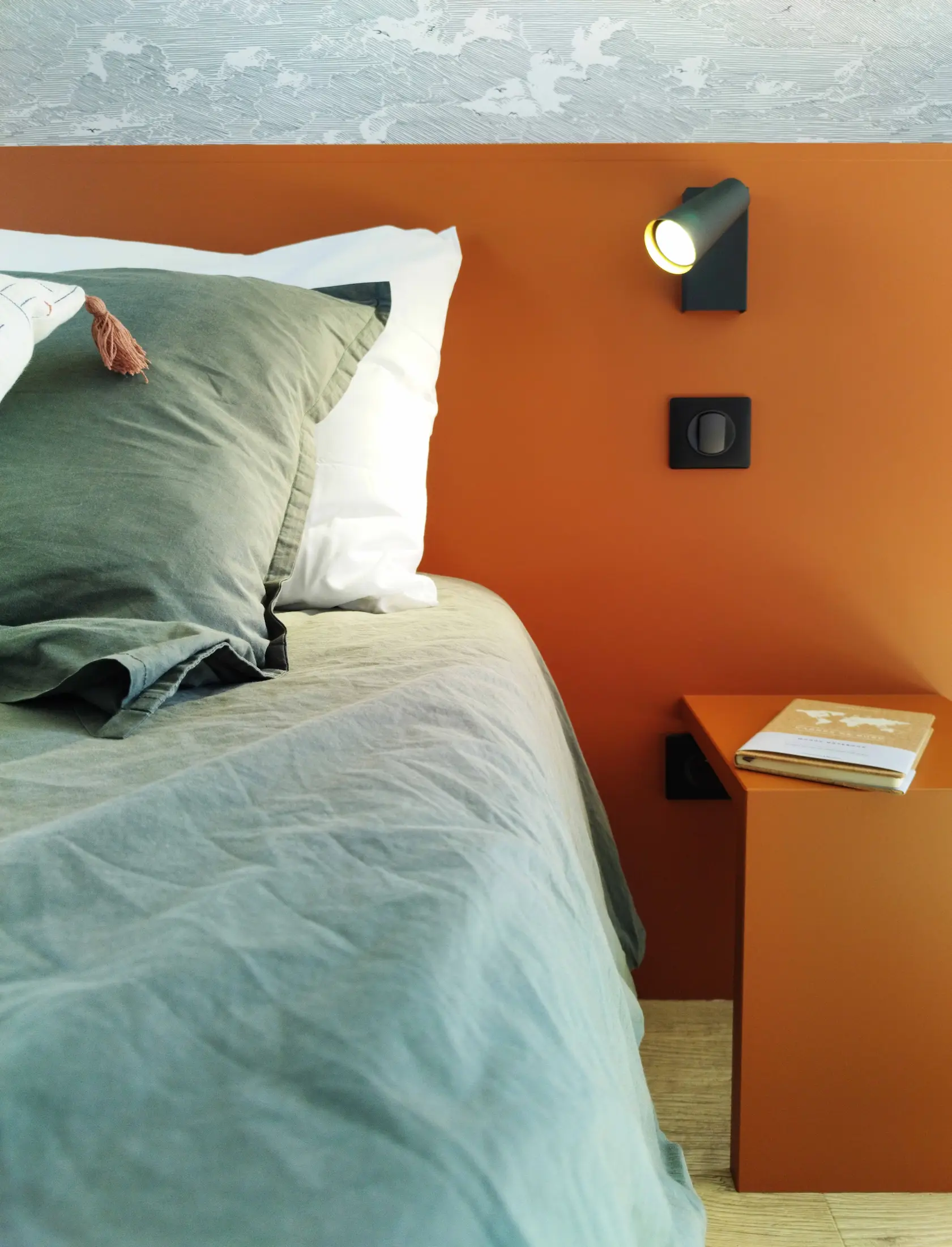 Zoom sur la tête de lit terracotta et l’éclairage mural noir dans la chambre redessinée avec un style chaleureux.