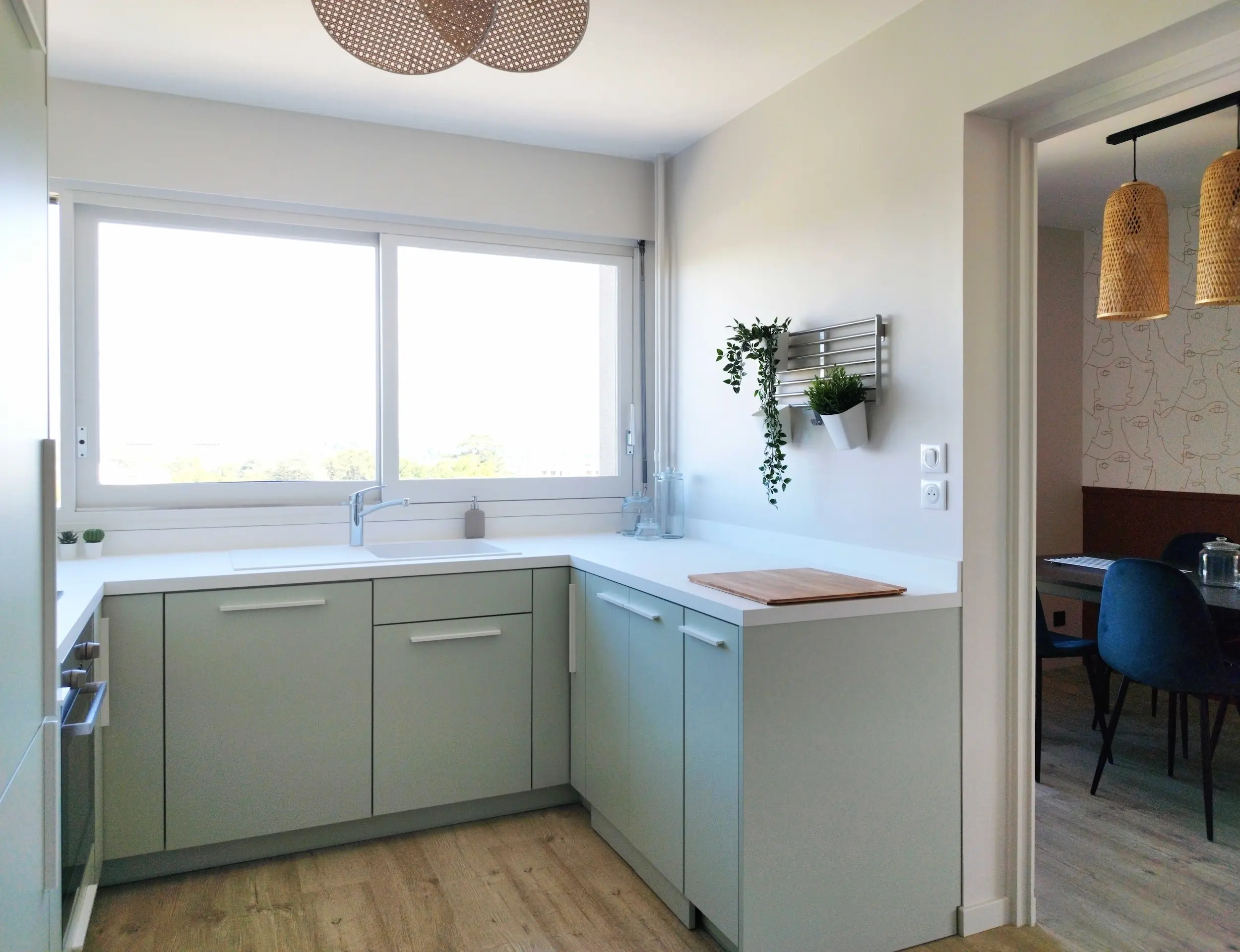 Cuisine sur-mesure en ton pastel avec grand plan de travail, baignée de lumière naturelle après la rénovation complète.