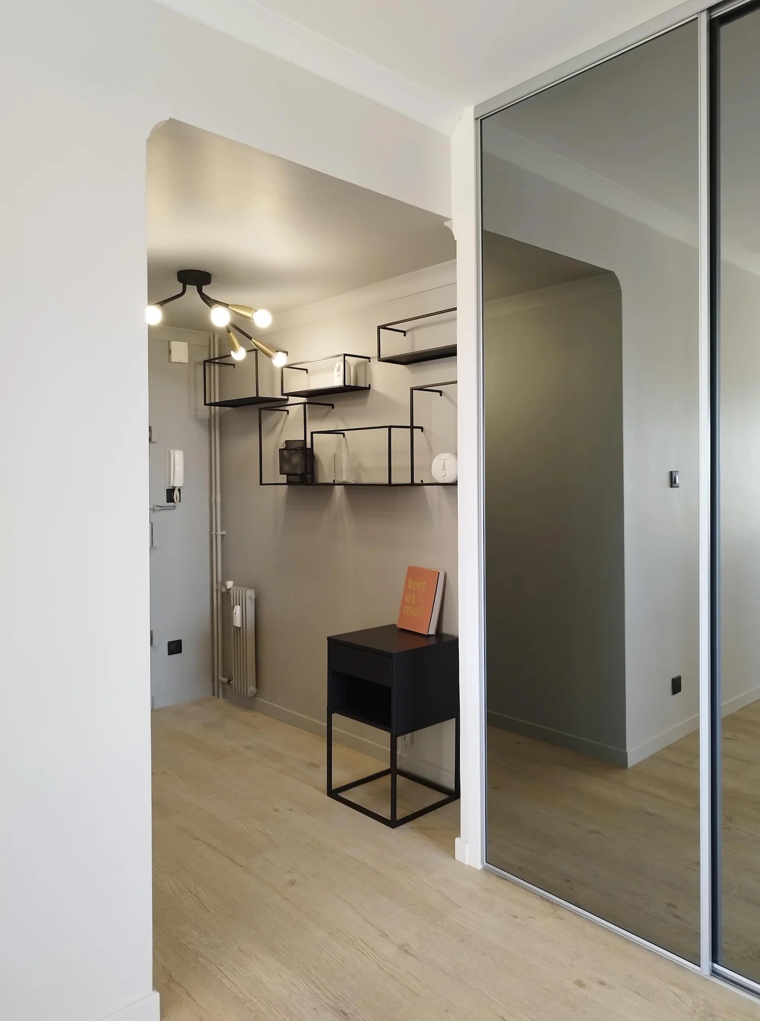 Entrée rénovée avec placard miroir, étagères métalliques et sol en bois clair, projet de restructuration d’appartement par Valentine.