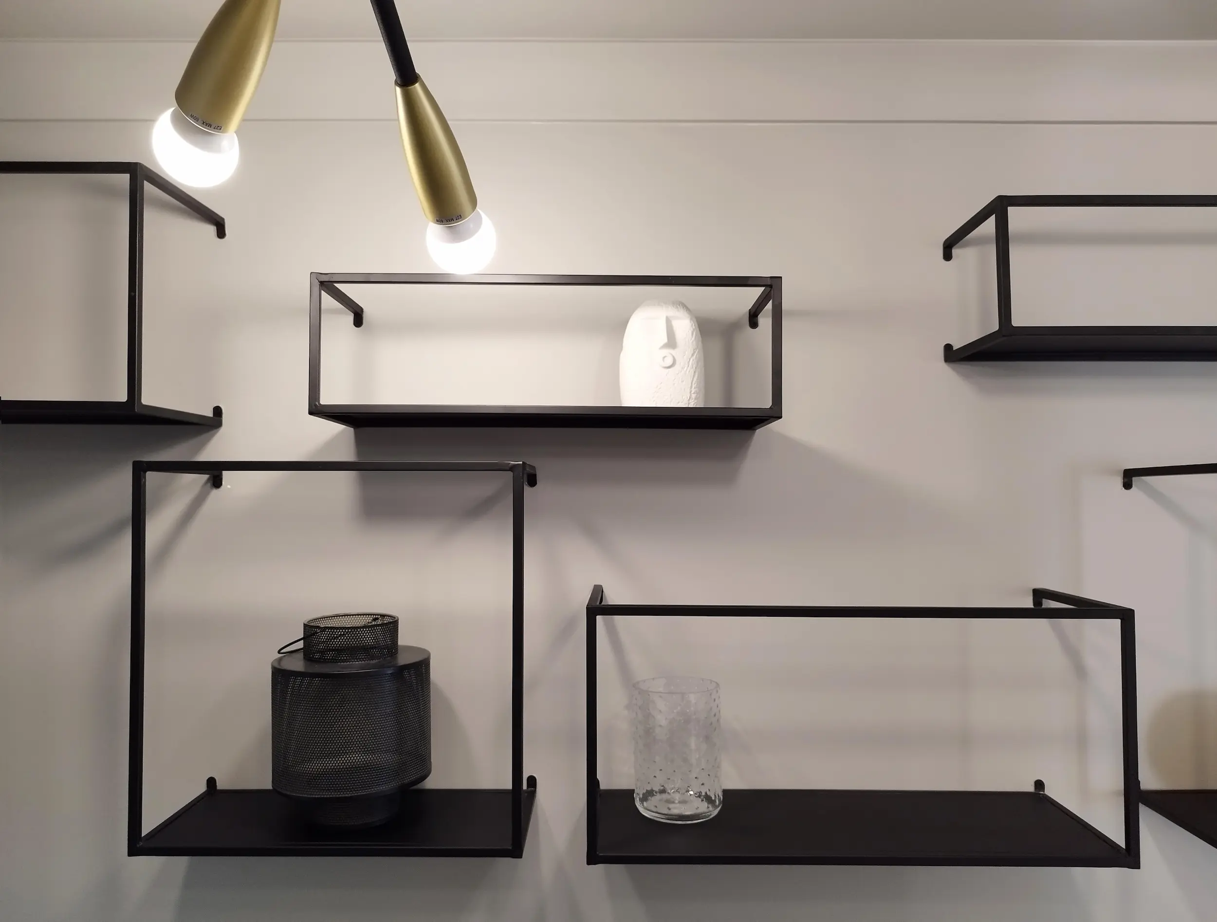 Détail des étagères murales en métal noir accueillant des objets décoratifs dans l’entrée.