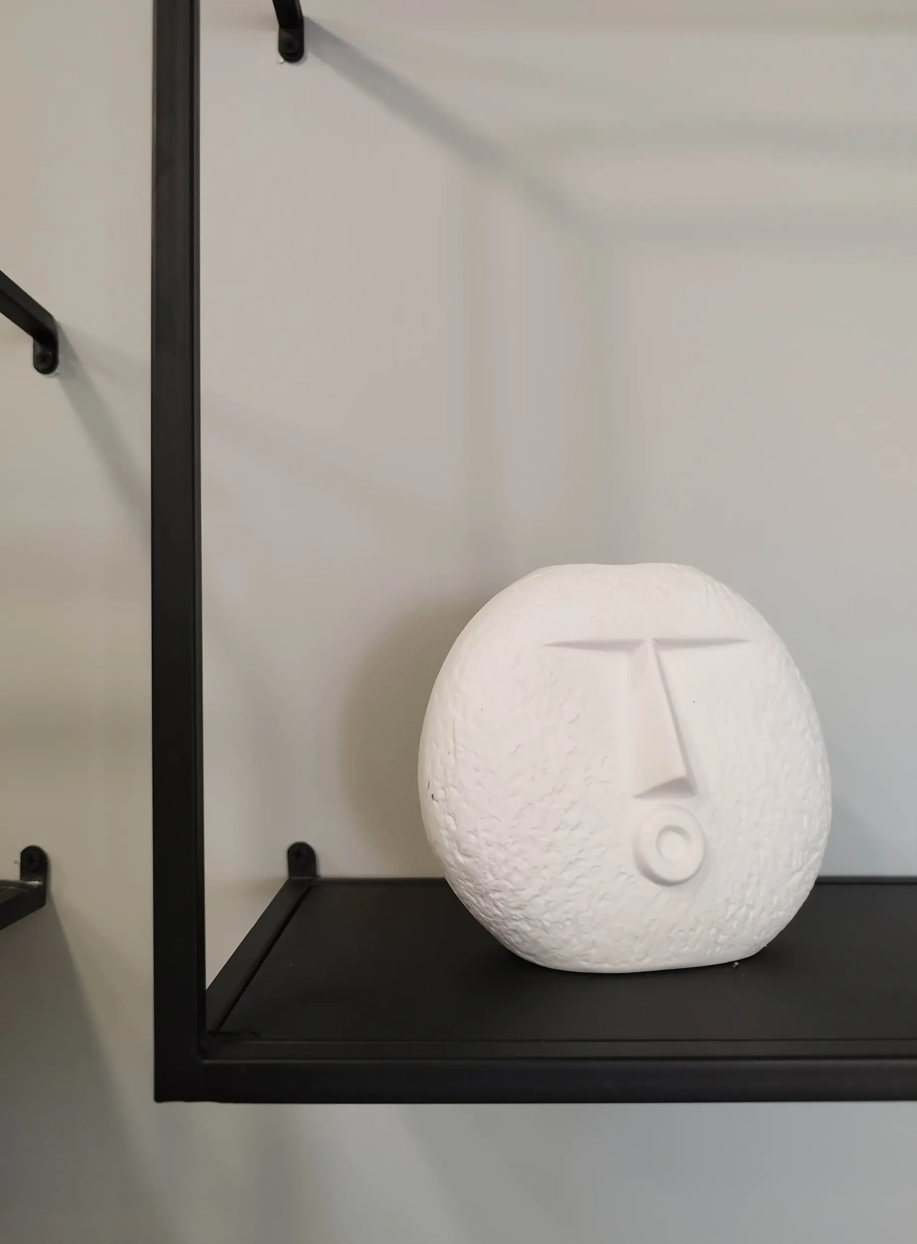 Objet décoratif en céramique blanche posé sur une étagère métallique noire dans l’entrée rénovée.