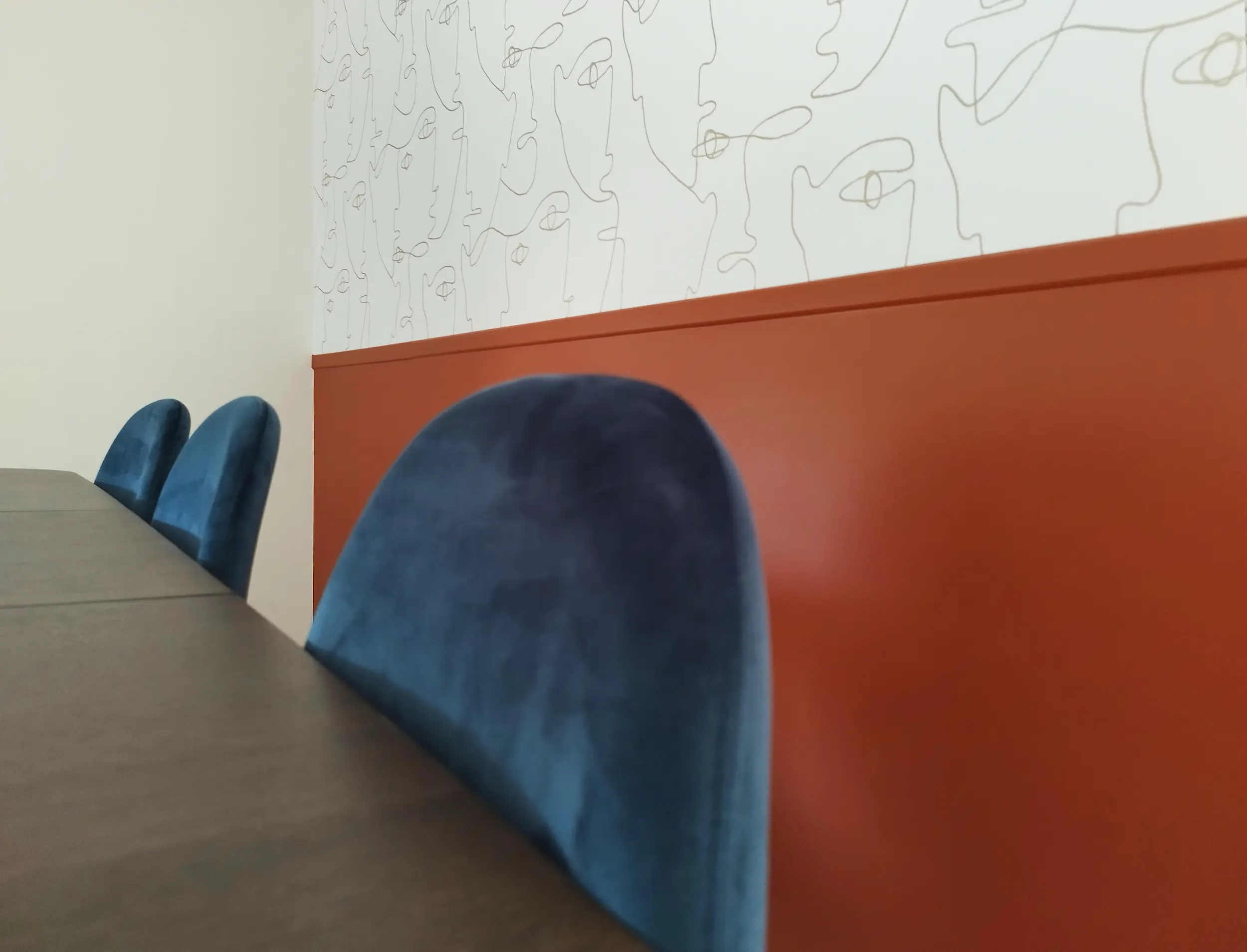 Alignement de dossiers de chaises bleu nuit le long d’un mur coloré surmonté d’un papier peint graphique.