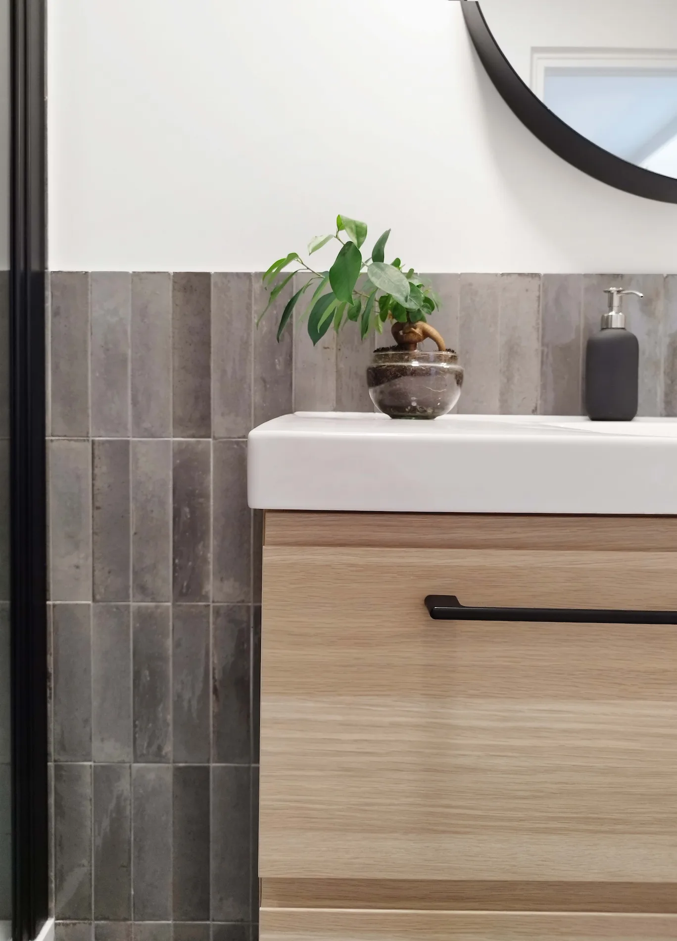 Vasque blanche avec meuble bois clair, robinet noir et petite plante verte en décoration.