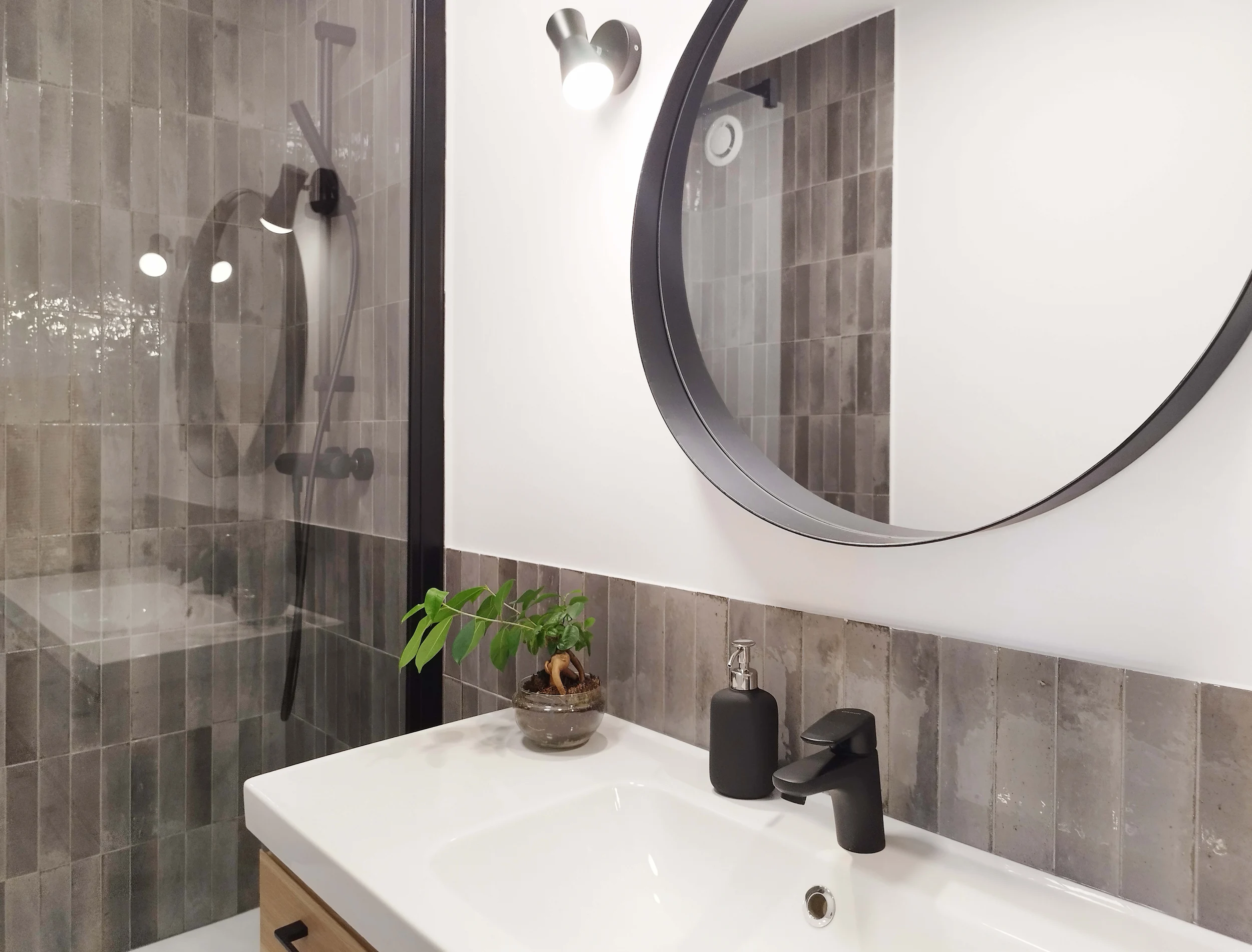 Plan rapproché sur le meuble vasque, grand miroir rond et faïence grise dans la salle de bain.