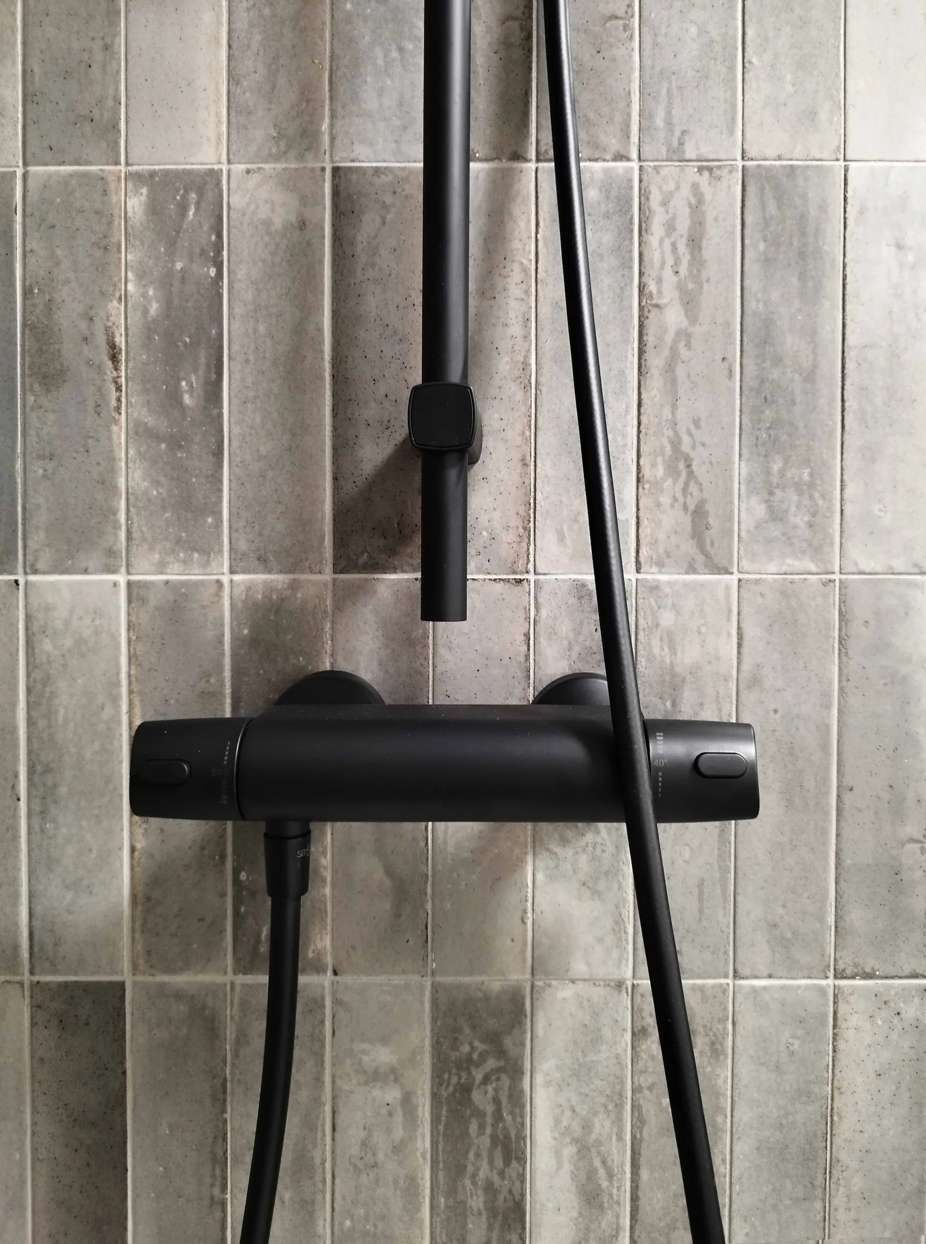 Mitigeur de douche noir mat sur carrelage gris vertical, détail de la robinetterie.