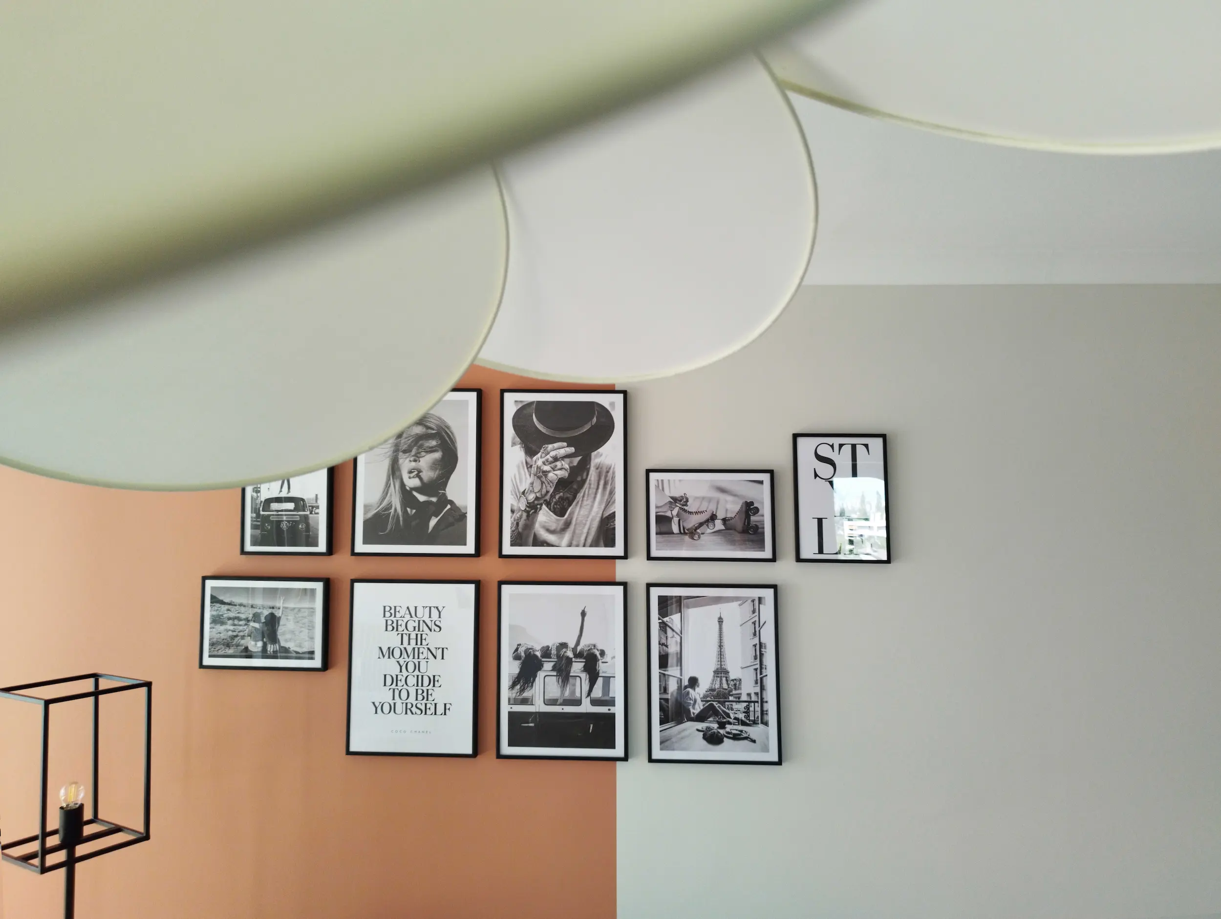 Mur de cadres noir et blanc sur fond coloré, partiellement cadré par une suspension design, projet signé Valentine Bourdier, architecte d’intérieur à Lyon.