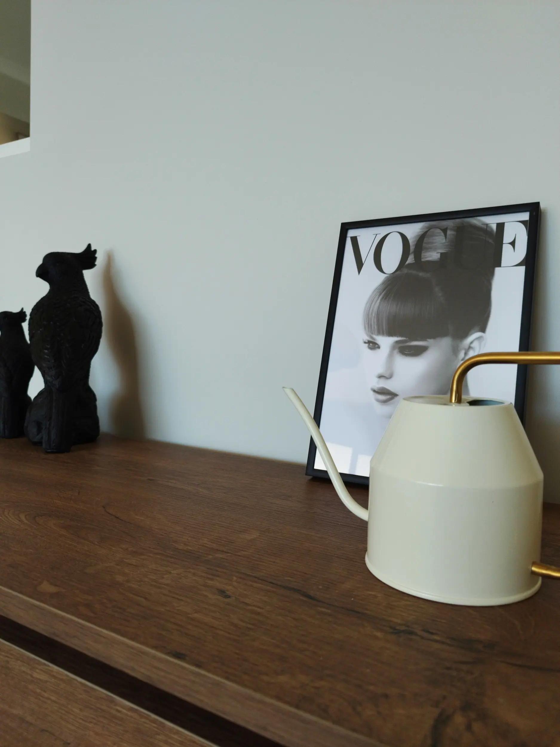 Zoom sur un arrosoir design blanc et un cadre Vogue posés sur un buffet en bois.