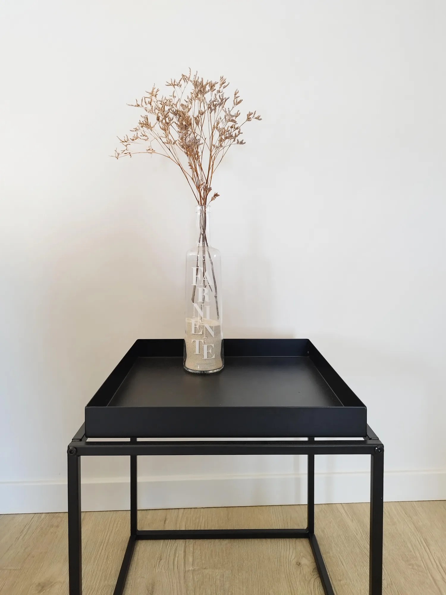 Table d’appoint noire mettant en valeur un vase transparent contenant des fleurs séchées.