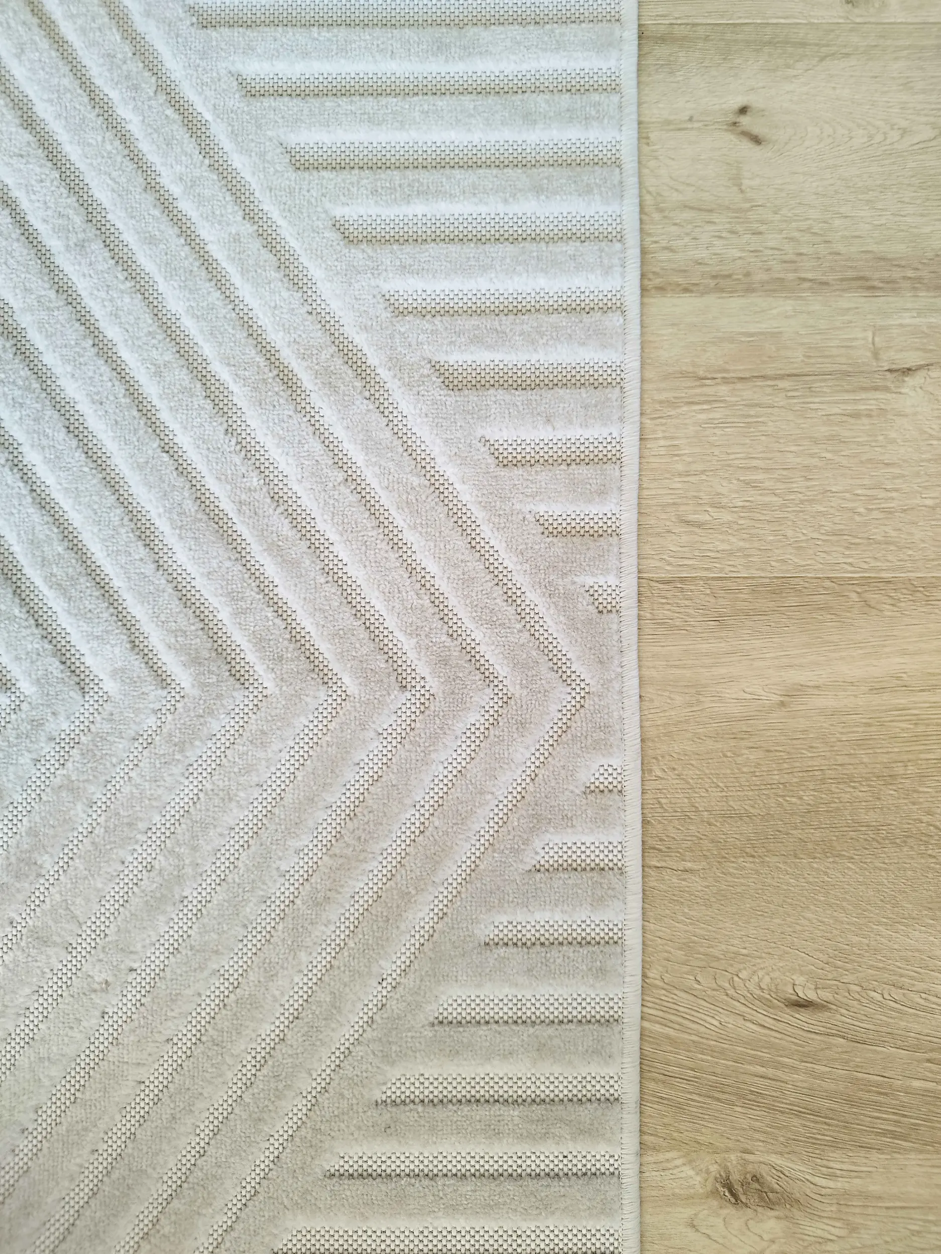 Détail d’un tapis texturé aux motifs géométriques en harmonie avec le parquet clair du salon.