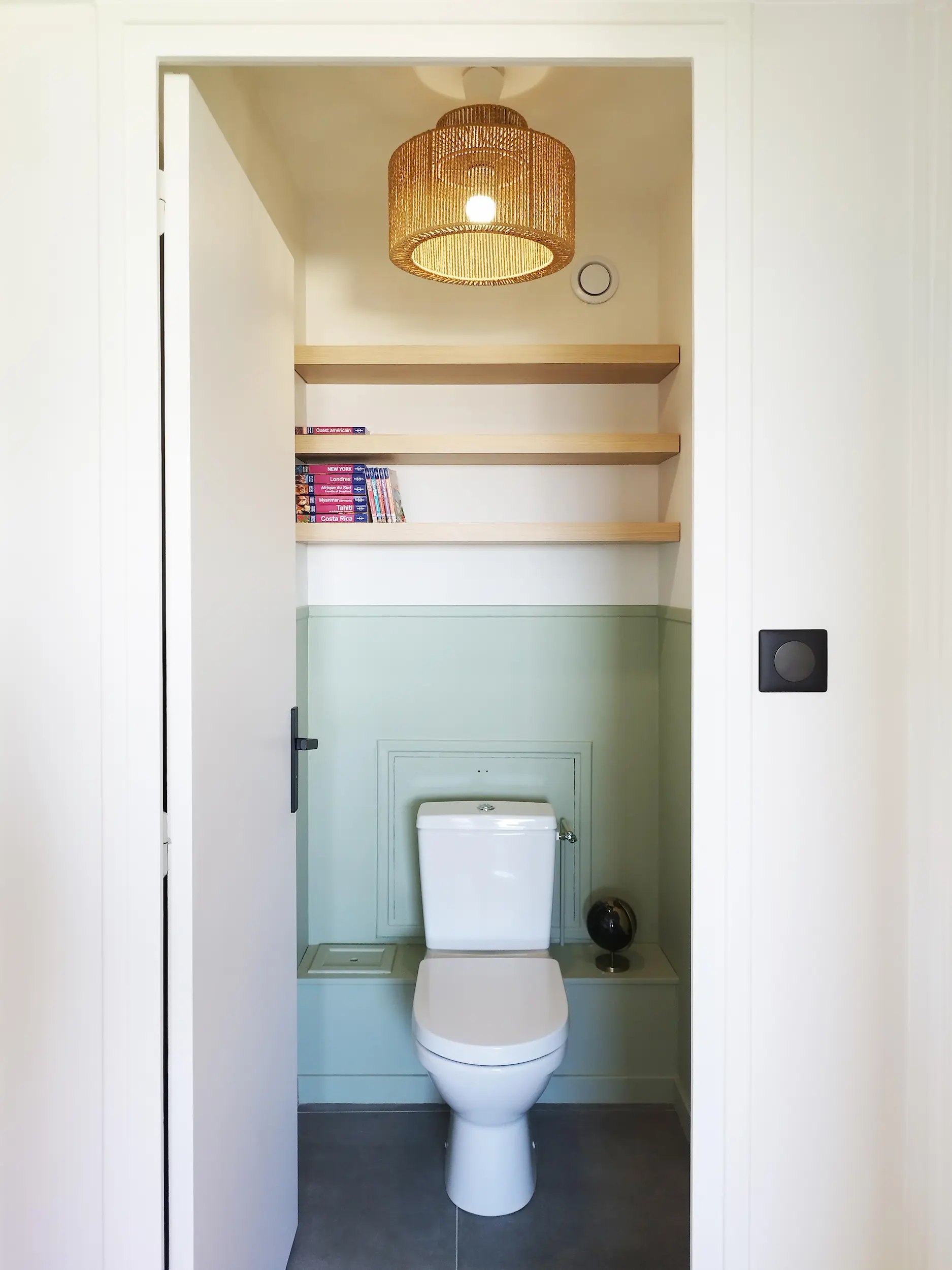 Petit espace WC réaménagé avec demi-peinture, étagères en bois et suspension naturelle pour une ambiance douce.
