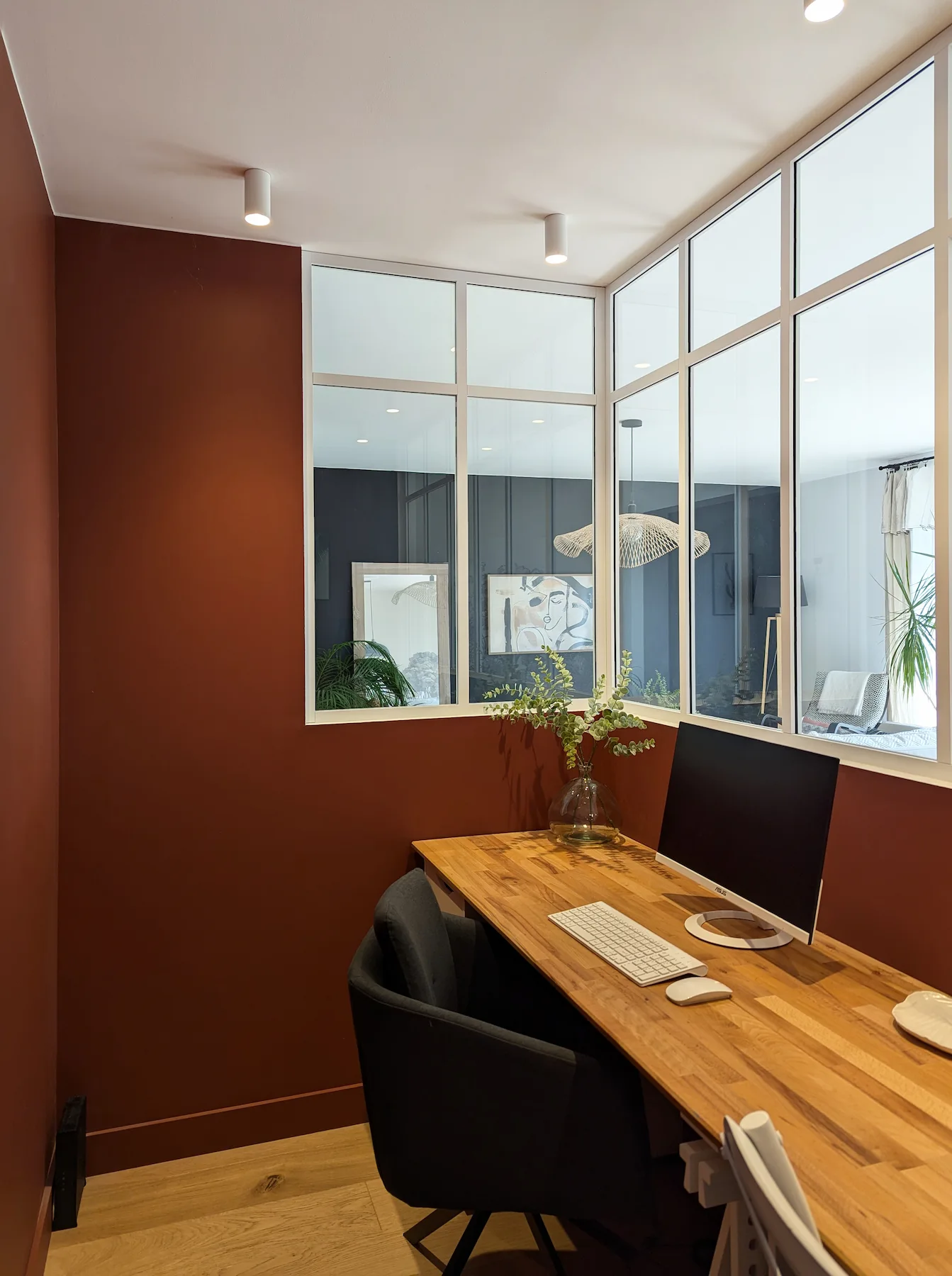 Espace bureau séparé par une verrière blanche, murs terracotta et mobilier en bois, conçu pour le télétravail dans un appartement familial.