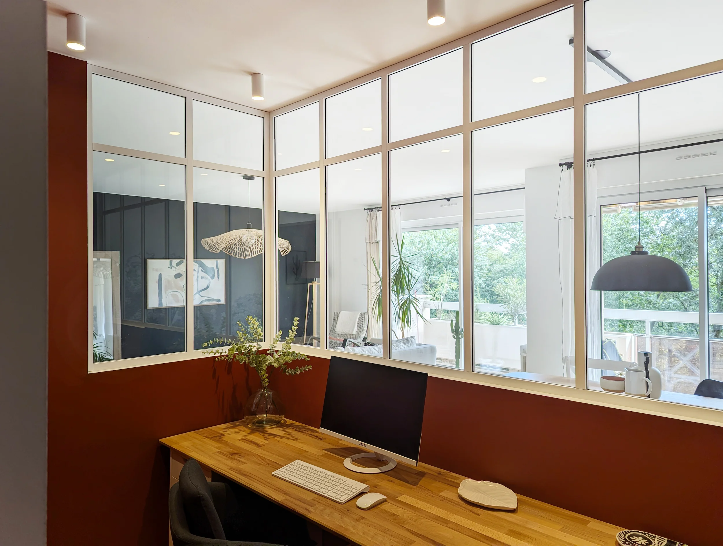 Espace bureau séparé par une verrière intérieure, avec plan de travail en bois.