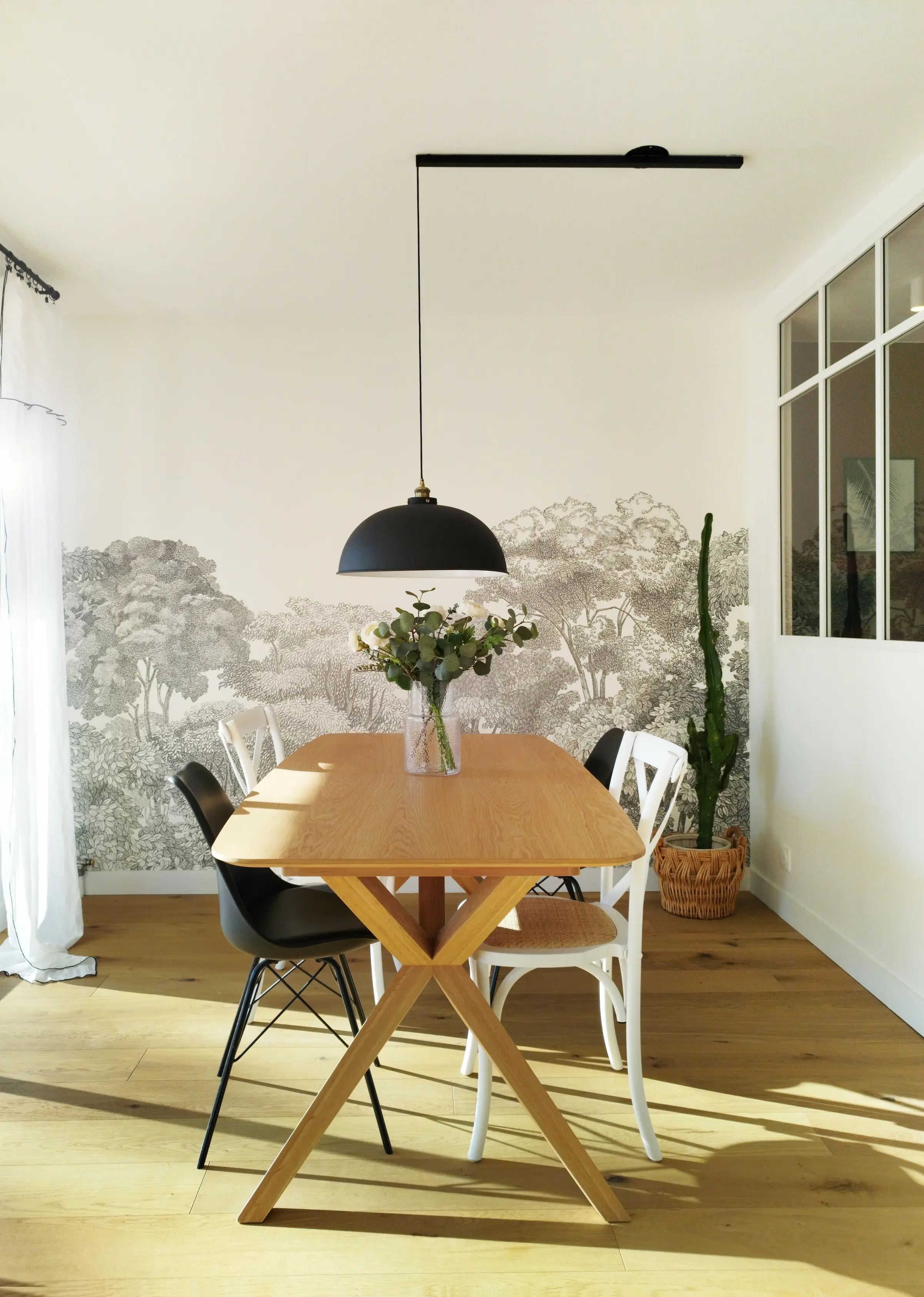 Salle à manger rénovée avec table en bois, suspension noire et papier peint panoramique, dans un appartement familial lyonnais.