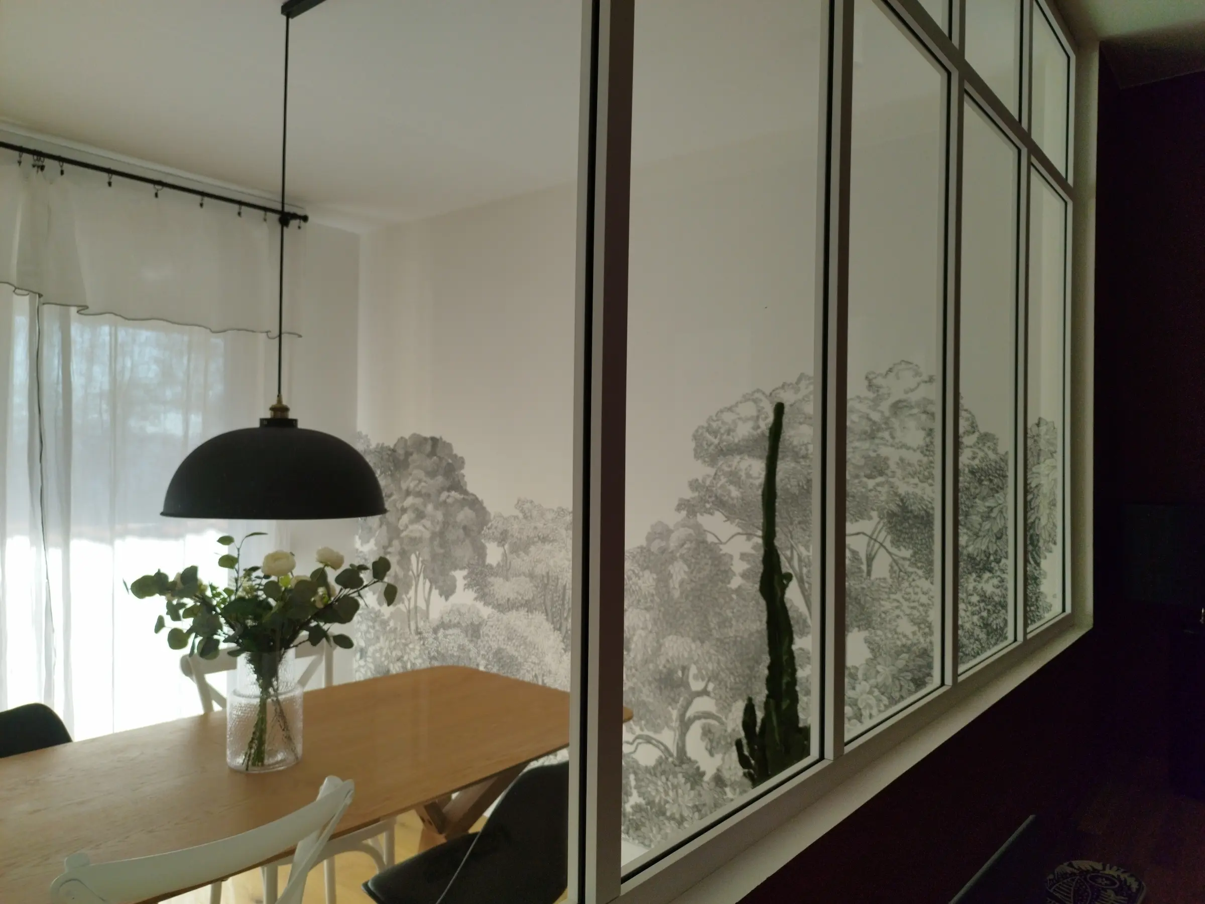 Vue à travers la verrière blanche séparant bureau et salle à manger, apportant la lumière en second jour dans l’appartement rénové.