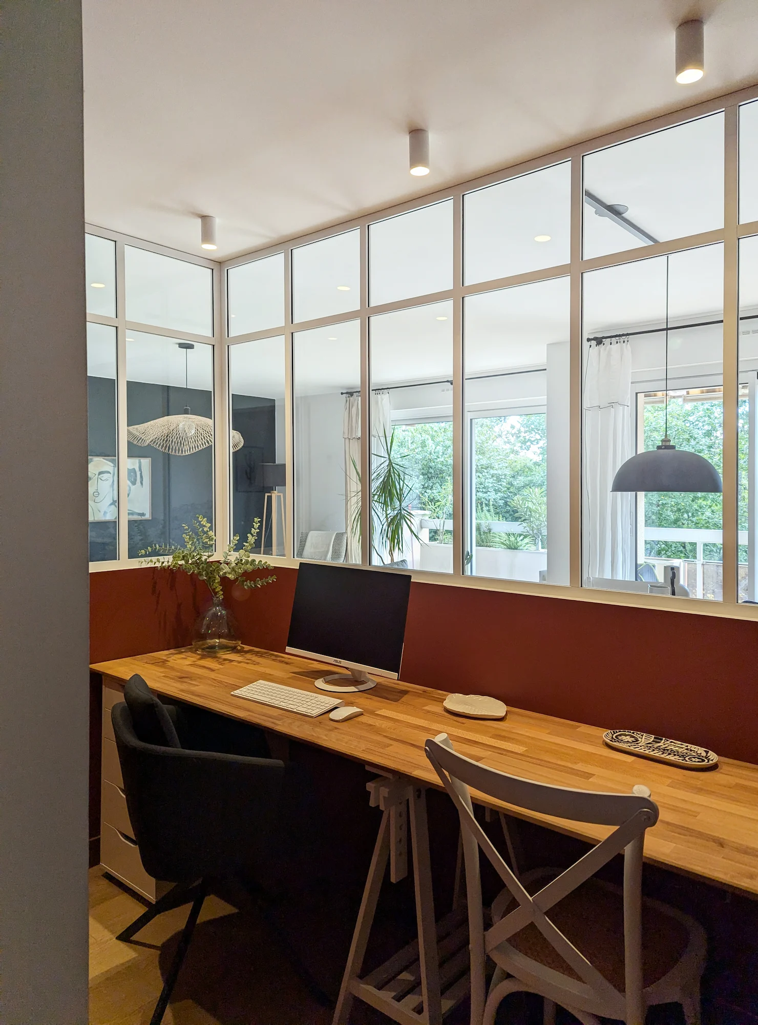Grand bureau partagé avec plan de travail en bois, chaises noires et verrière intérieure, aménagement pensé pour le télétravail familial.