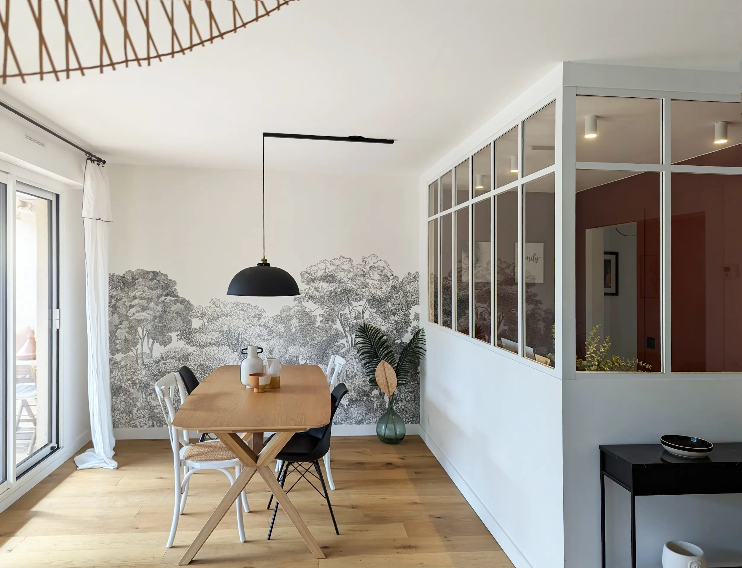 Vue d’ensemble de la salle à manger rénovée avec verrière intérieure, suspension noire et sol en bois, projet de réhabilitation d’un appartement des années 70.