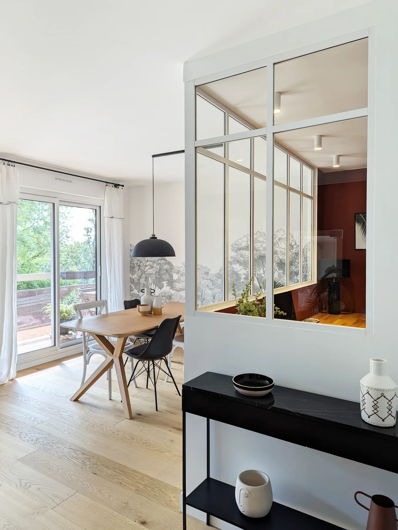 Salle à manger lumineuse avec verrière blanche et table en bois, aménagement intérieur par l’agence Jiwa.a.