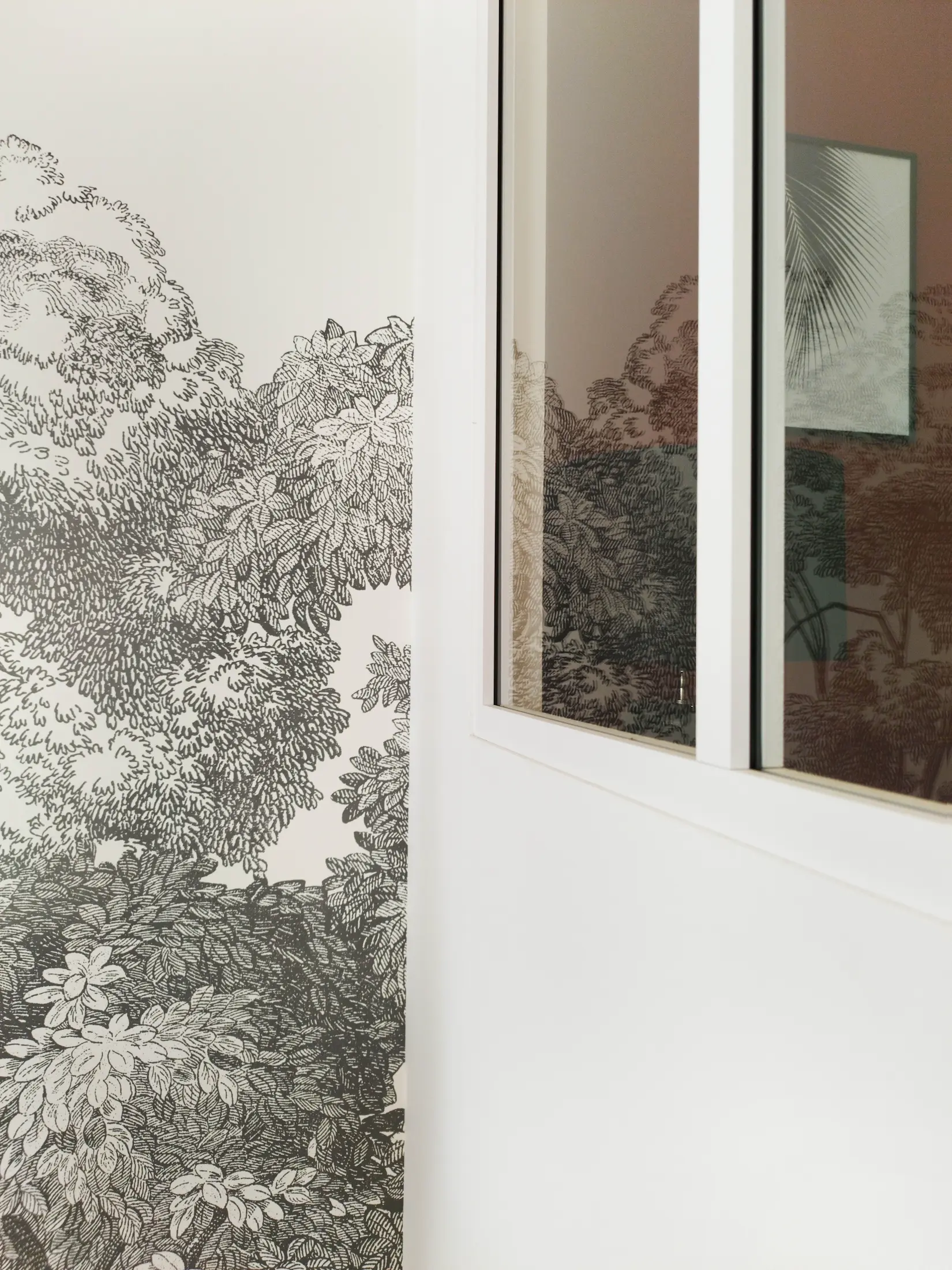 Détail du papier peint panoramique végétal et de la verrière blanche, apportant texture et profondeur à l’espace de vie.
