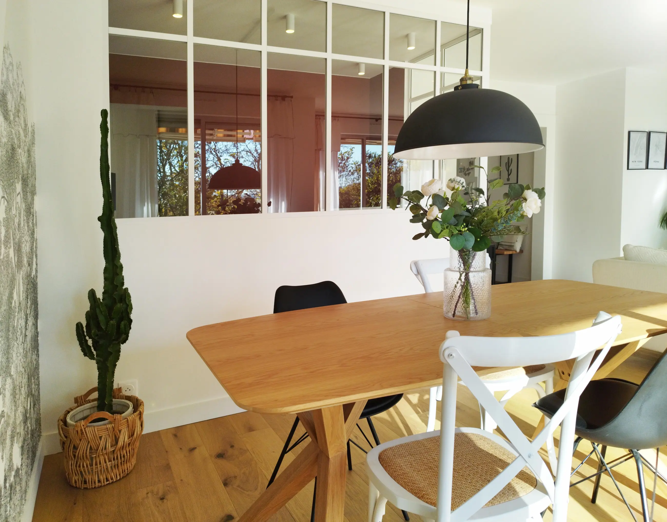 Salle à manger contemporaine avec table en bois, chaises dépareillées, verrière blanche et papier peint panoramique, projet signé Valentine Bourdier.