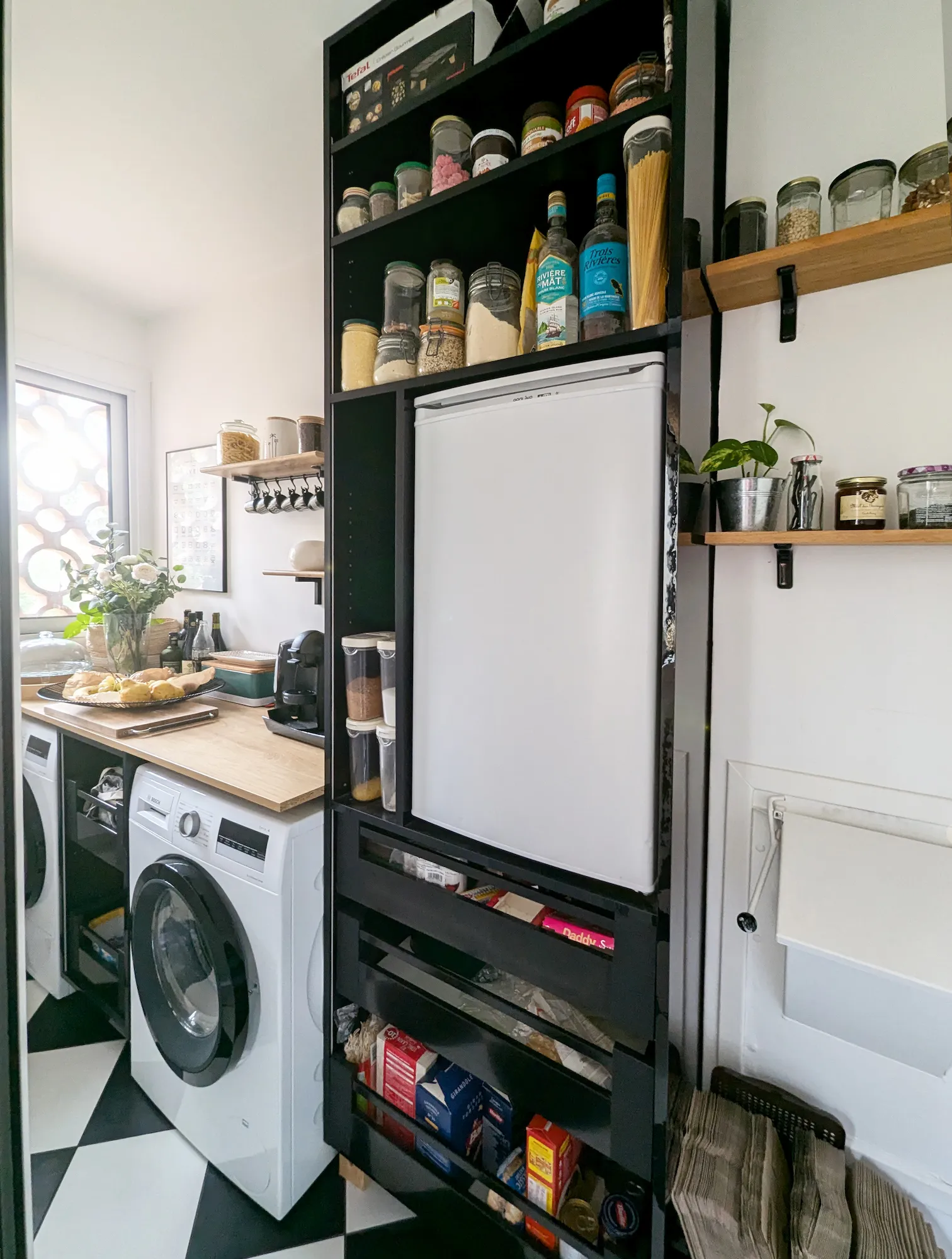 Cellier optimisé avec rangements ouverts, étagères murales et intégration du lave-linge, dans un appartement familial rénové des années 70.