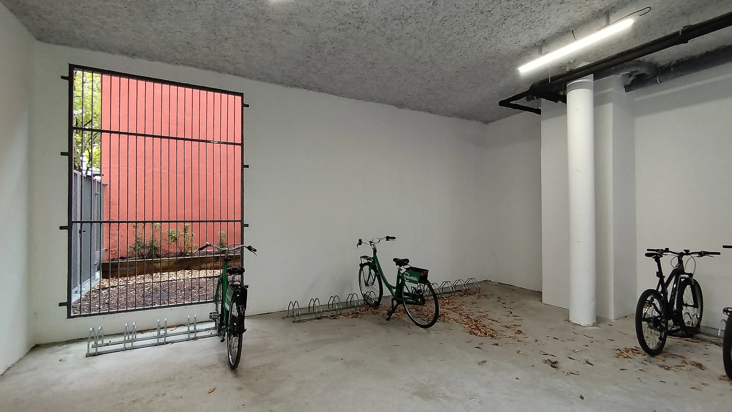 Local vélo avant décoration, avec sol béton, murs blancs, stationnement de vélos et ouverture sécurisée sur l’extérieur, à Villeurbanne.