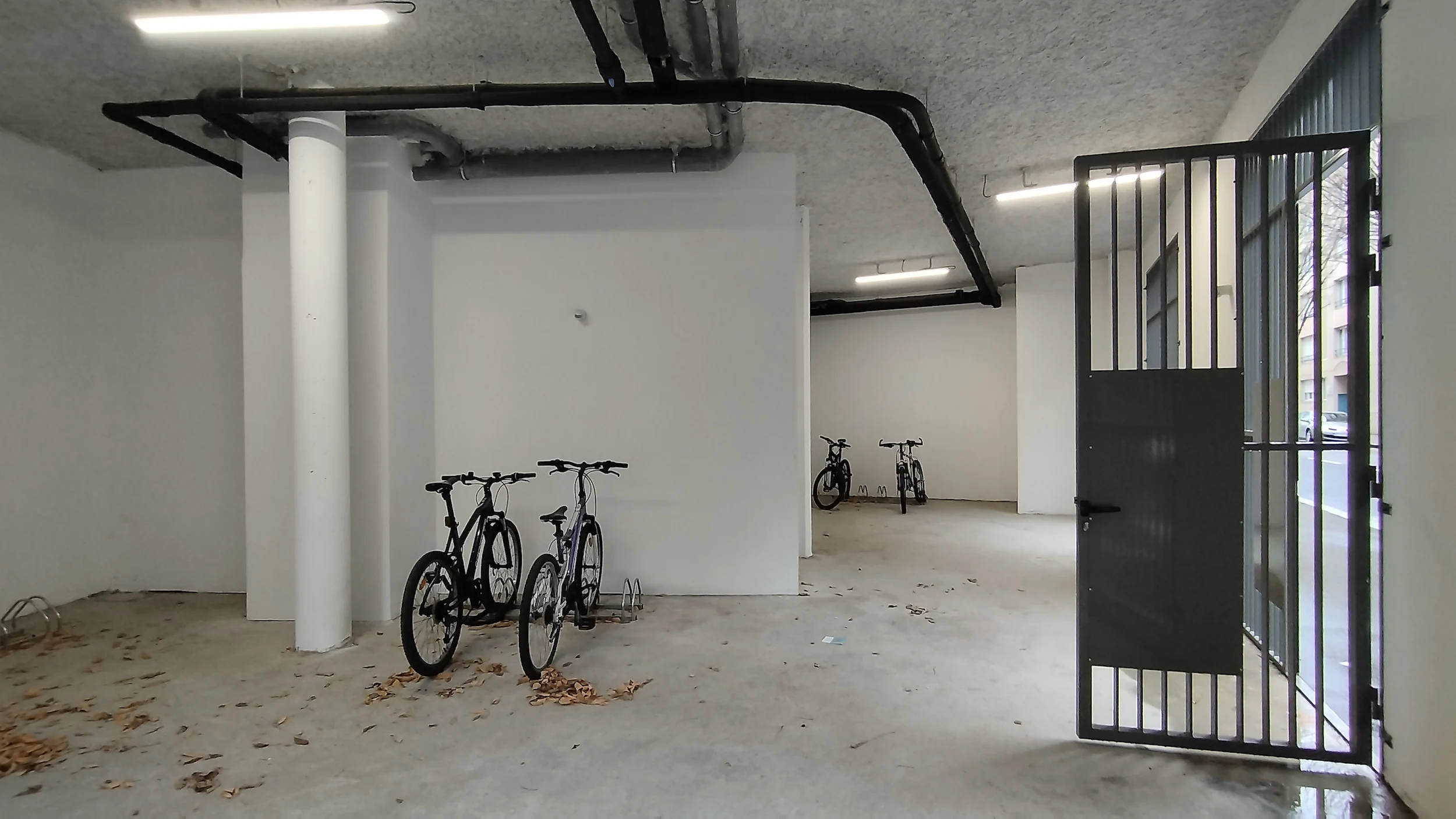 Vue intérieure du local vélo avec portes métalliques, vélos stationnés et éclairage linéaire au plafond, état existant avant décoration.
