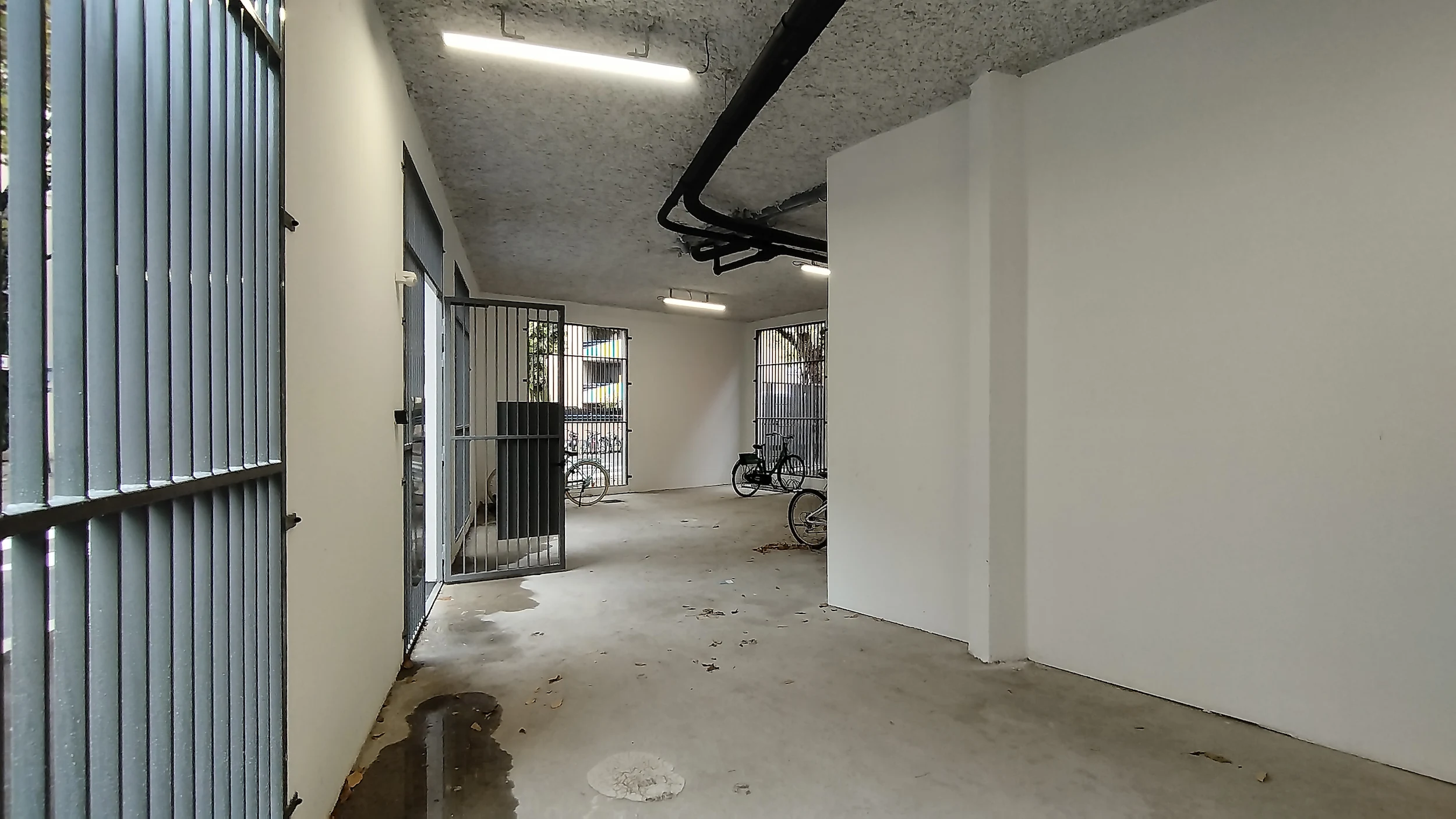 Circulation intérieure du local vélo avec murs blancs, sol brut et accès sécurisé, espace commun situé en plein cœur de la région lyonnaise.