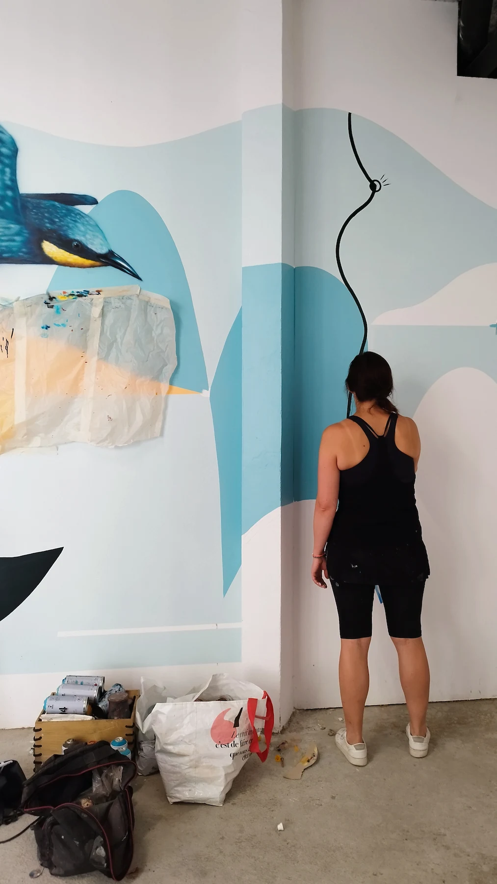 Artiste peignant une fresque murale abstraite aux tons bleus dans un local vélo, collaboration avec des artistes urbains locaux.