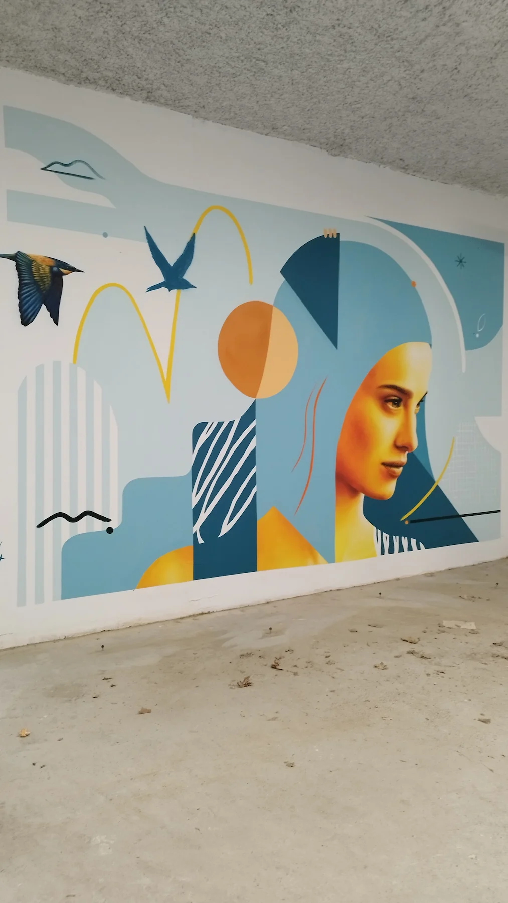 Vue d’ensemble d’une fresque murale colorée aux formes graphiques et visage stylisé, réalisée pour la décoration d’un local vélo.