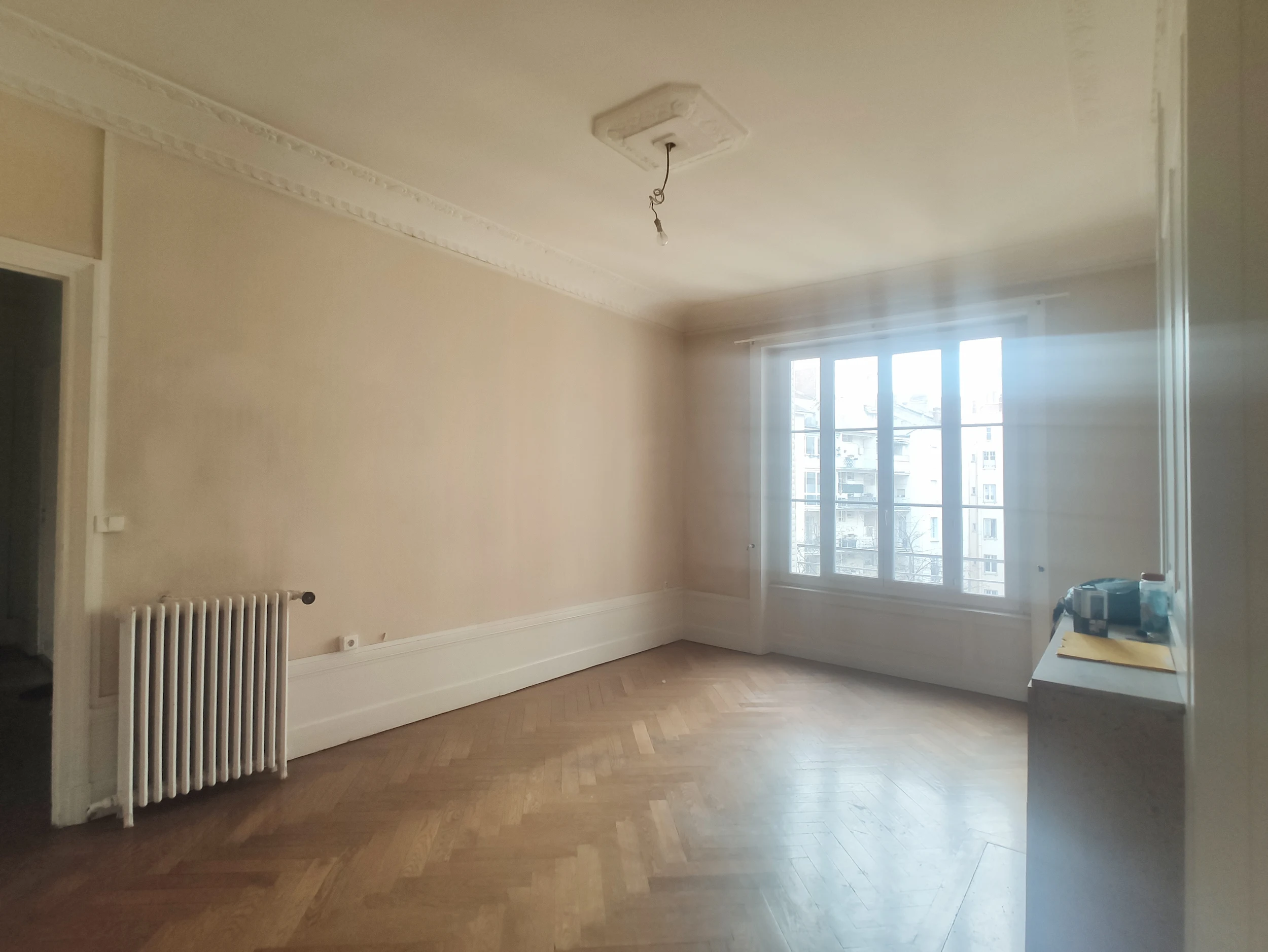 Pièce de vie avant rénovation avec parquet en chevrons et murs clairs.