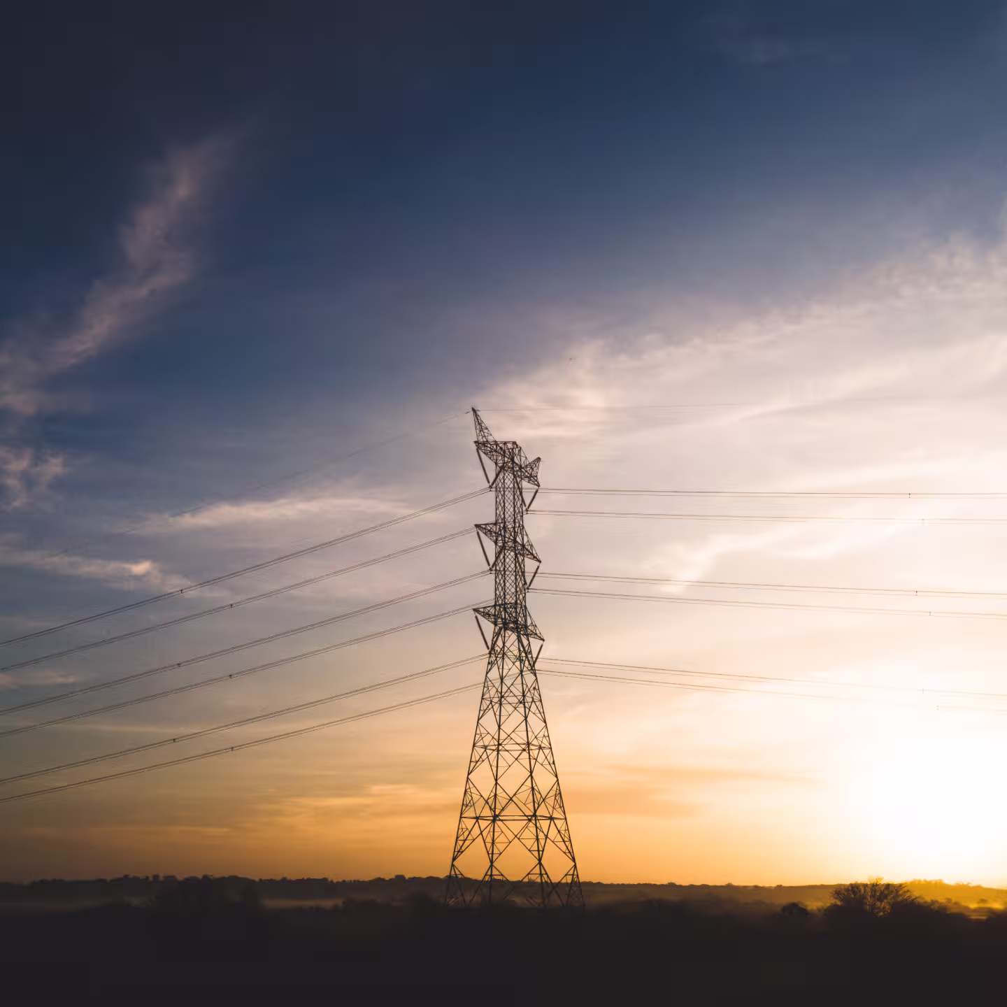 Electric transmission tower standing against a colorful sunset sky with scattered clouds.