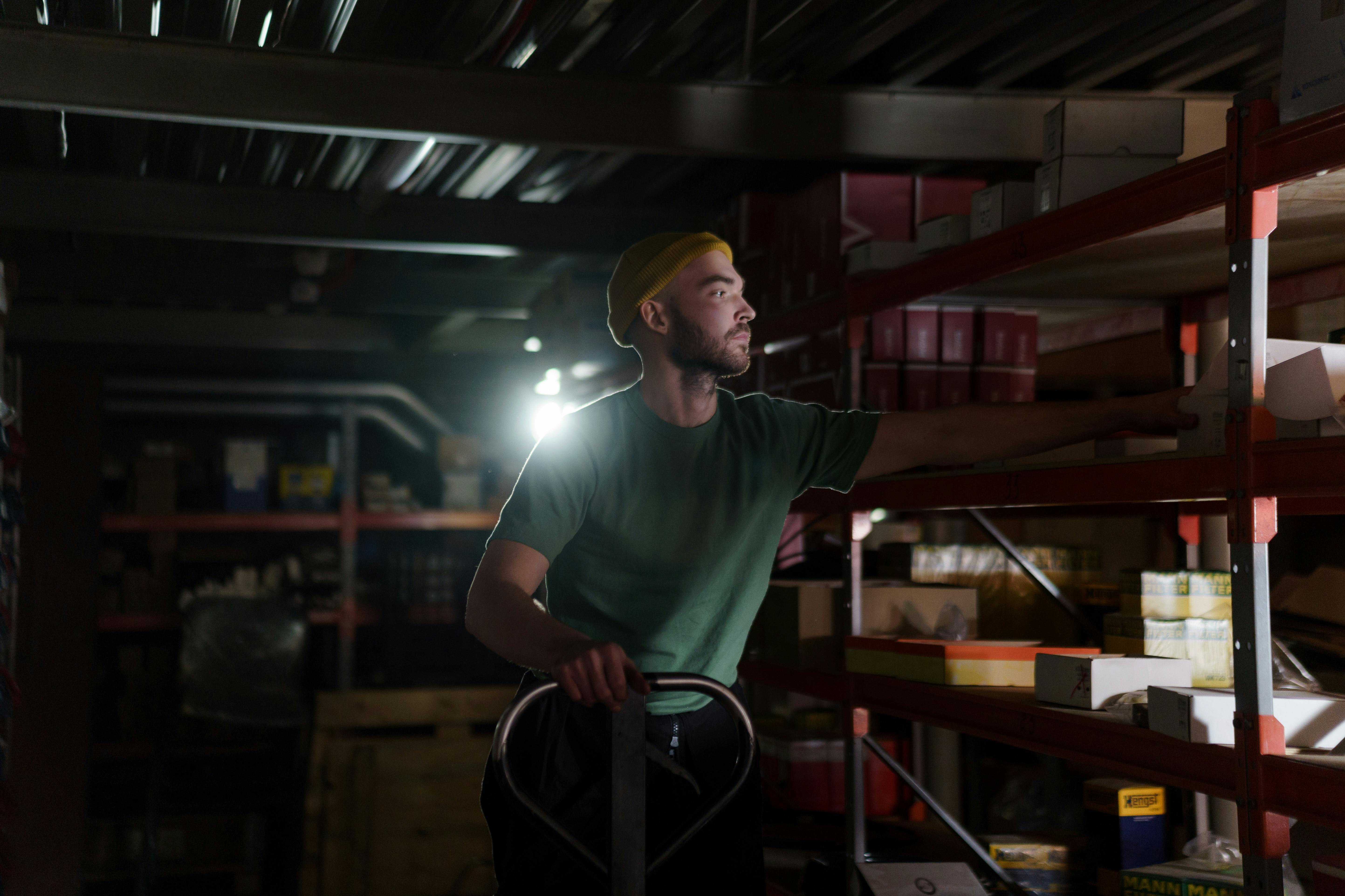 A warehouse worker pulling a box from a shelving unit, with a handheld cart and scanner in their other hand.
