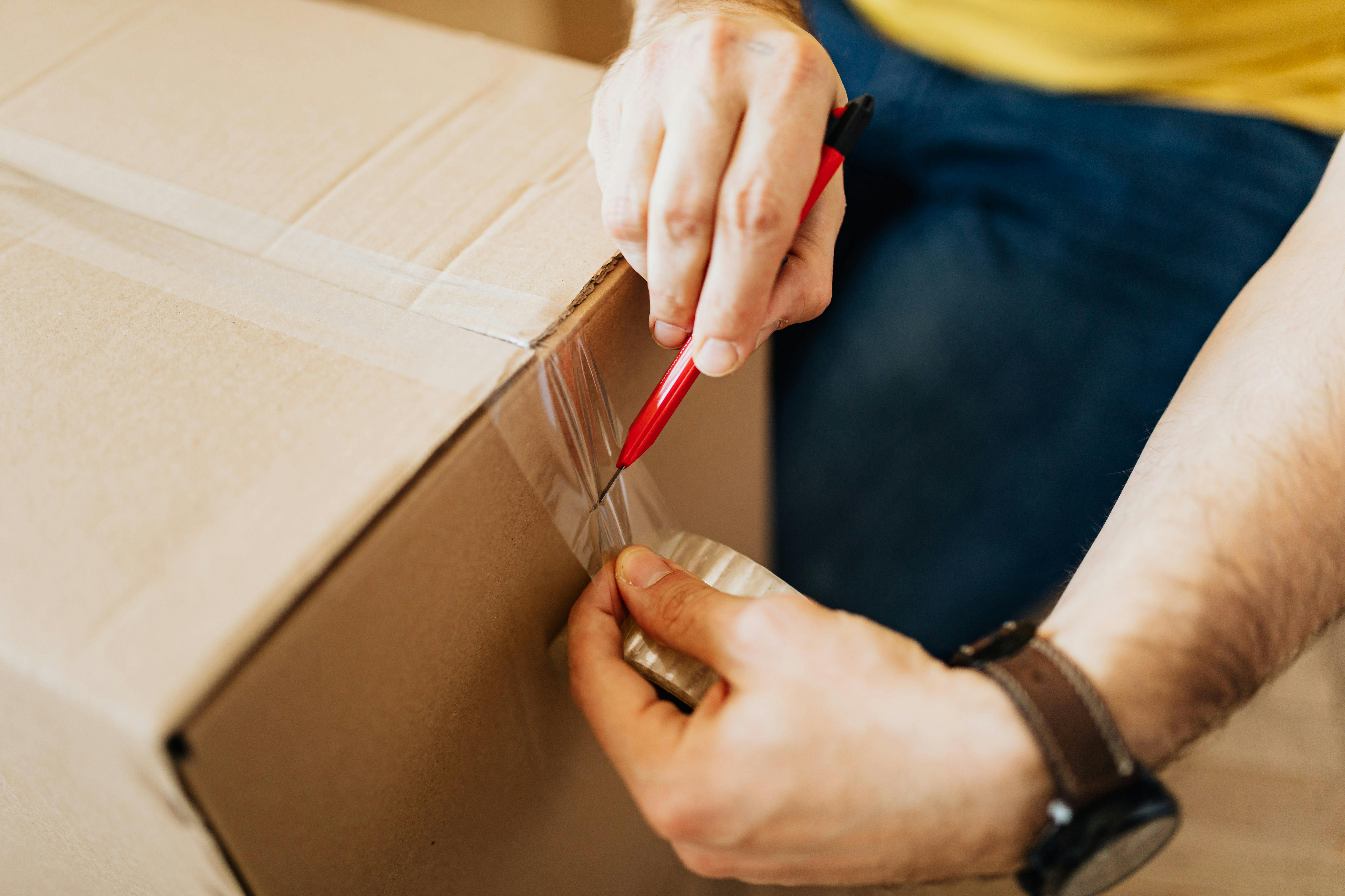 A worker taping up a cardboard box on a packing station, with labels and packing materials nearby.