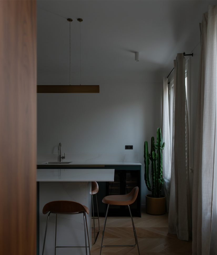 Minimalist kitchen corner with two wooden bar stools at a white marble counter, a tall cactus in a pot, and beige curtains on windows.