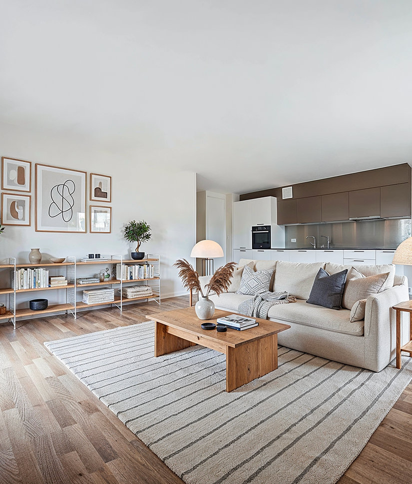 Bright modern living room with beige sofa, wooden coffee table, patterned rug, and minimalist shelving with books and decor.