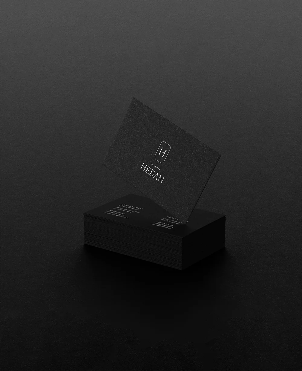 Stos czarnych wizytówek z białym logo i napisem GALERIA HEBAN na ciemnym tle.