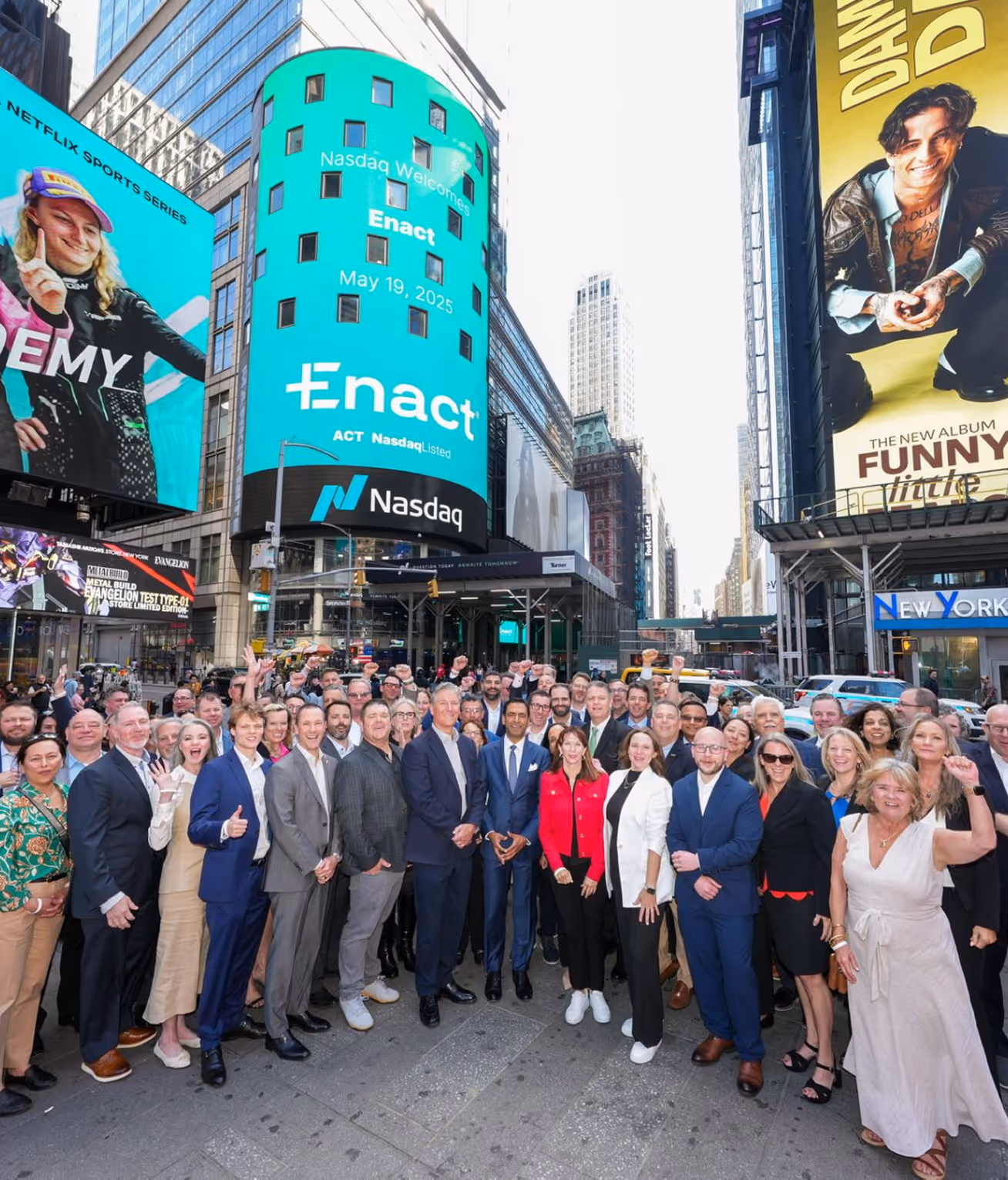 Large group of professionally dressed people posing in Times Square, New York City with Nasdaq digital billboard displaying 'Enact' behind them.
