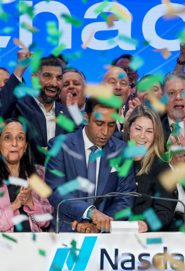 Group of diverse people celebrating with confetti as CEO - a man in a blue suit - presses a button at a Nasdaq event.