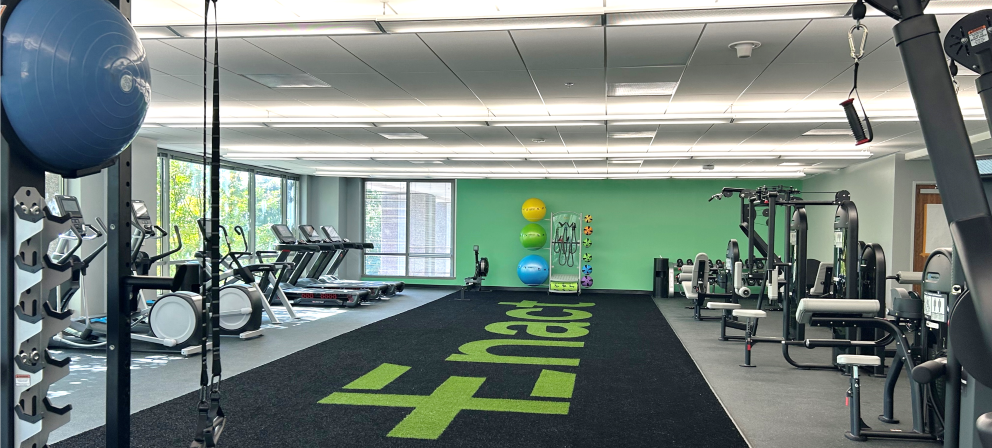 Spacious gym with treadmills, exercise bikes, weight machines, and colorful exercise balls against a green accent wall and Enact carpet.
