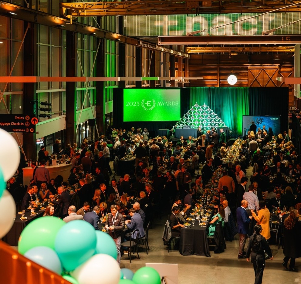 Group of diverse adults seated at round banquet tables, clapping and smiling during an indoor event.