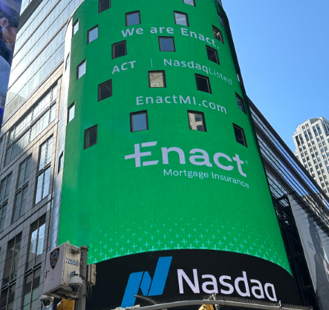 Two people wearing Enact t-shirts smiling and spinning a colorful prize wheel outside an office building.